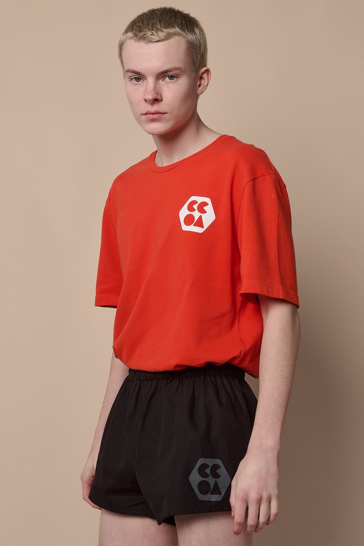 
            Thigh up image of white male wearing men&#39;s lightweight sports short plastic free in black with CCOA logo paired with breathable short sleeve t shirt in flame red.