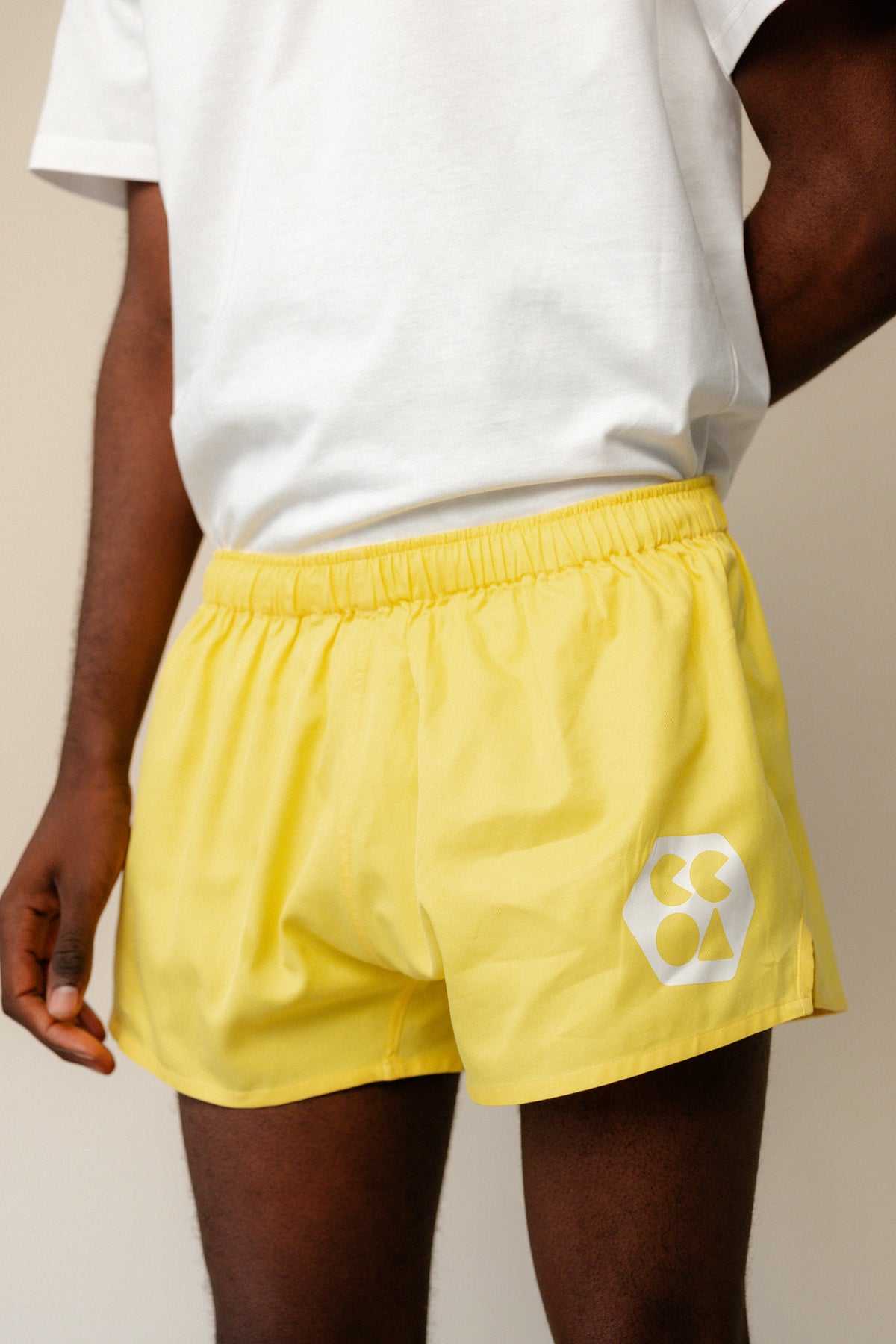 
            Male wearing lightweight sports short plastic free in canary yellow with white CCOA logo