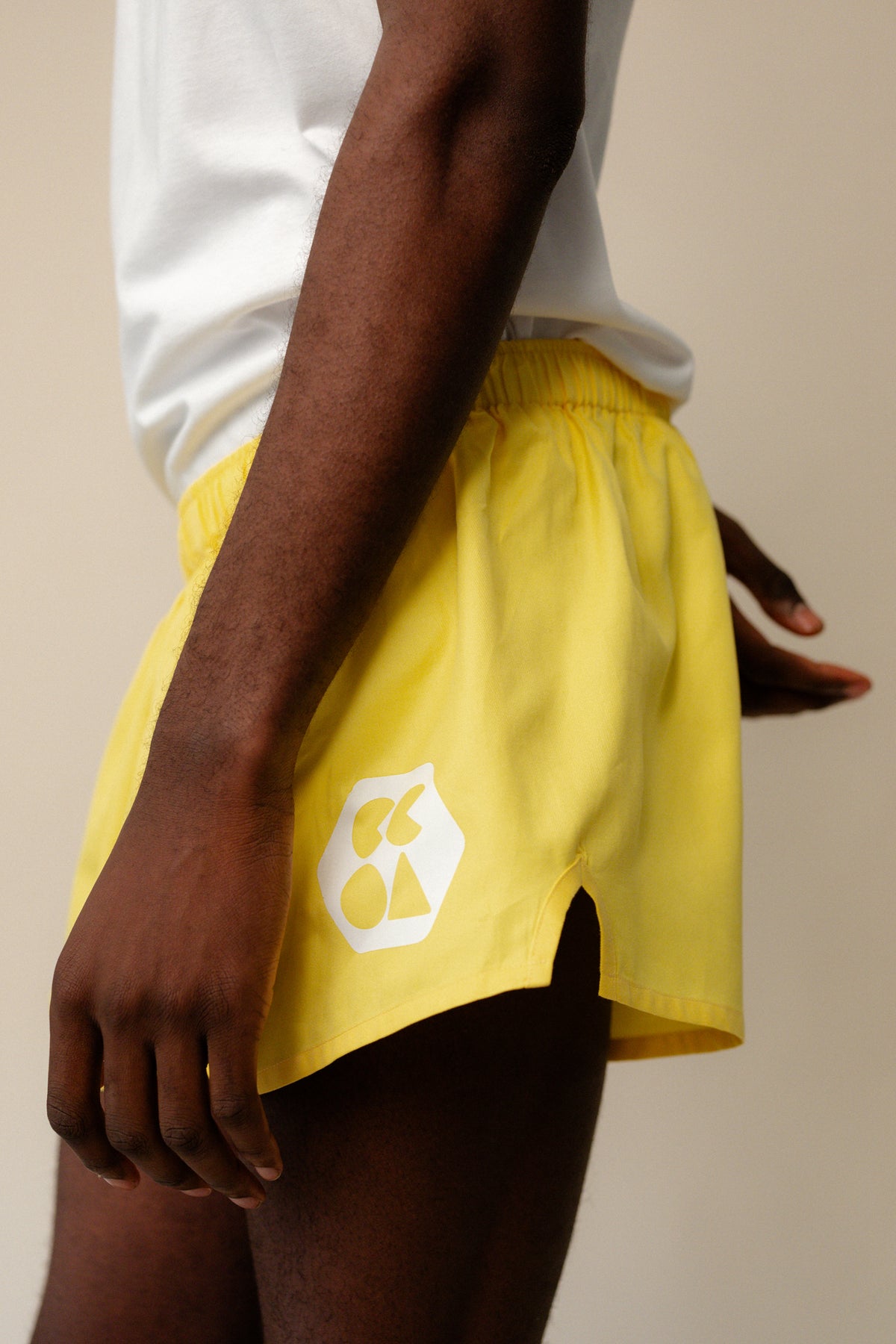 
            Shot of black male wearing men&#39;s lightweight sports short plastic free in canary yellow from the side showing white CCOA logo and elasticated waistband