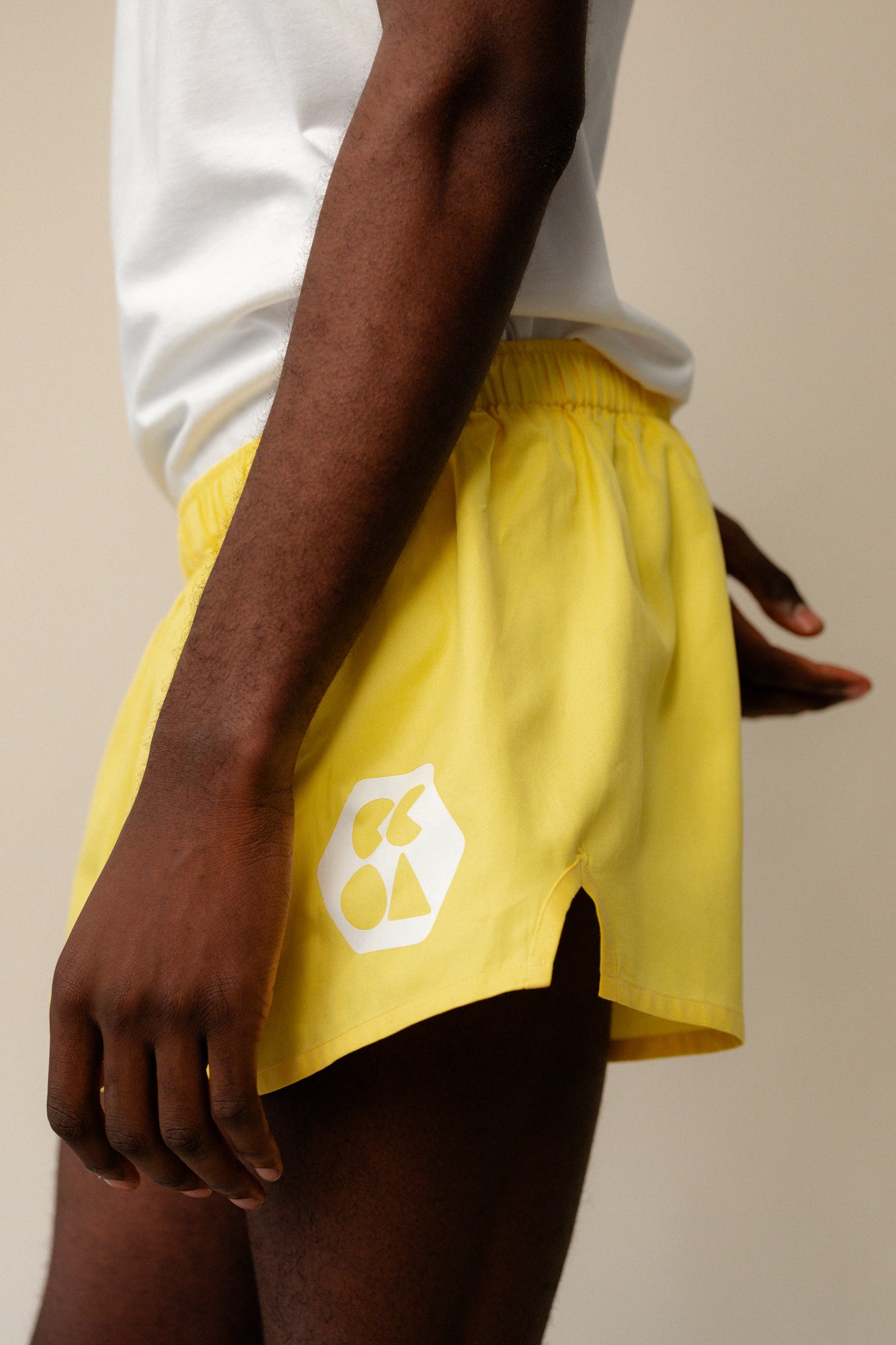 Shot of black male wearing men's lightweight sports short plastic free in canary yellow from the side showing white CCOA logo and elasticated waistband
