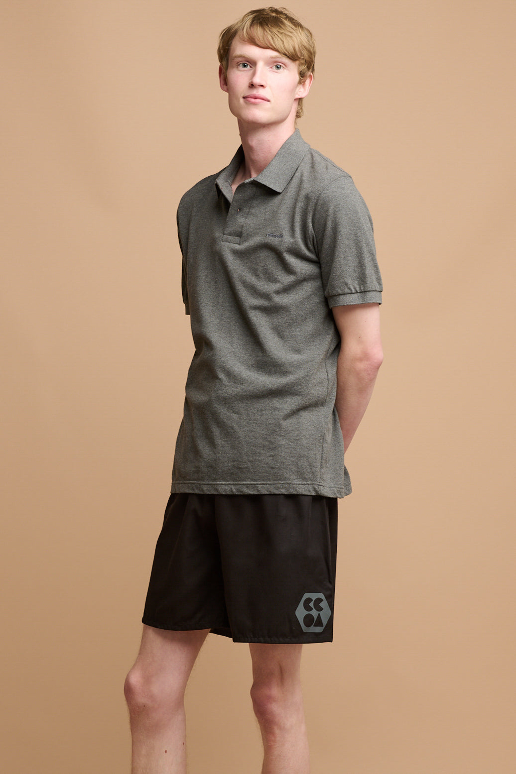 
            Blonde male wearing community polo shirt in grey paired with long lightweight running short in black with CCOA logo