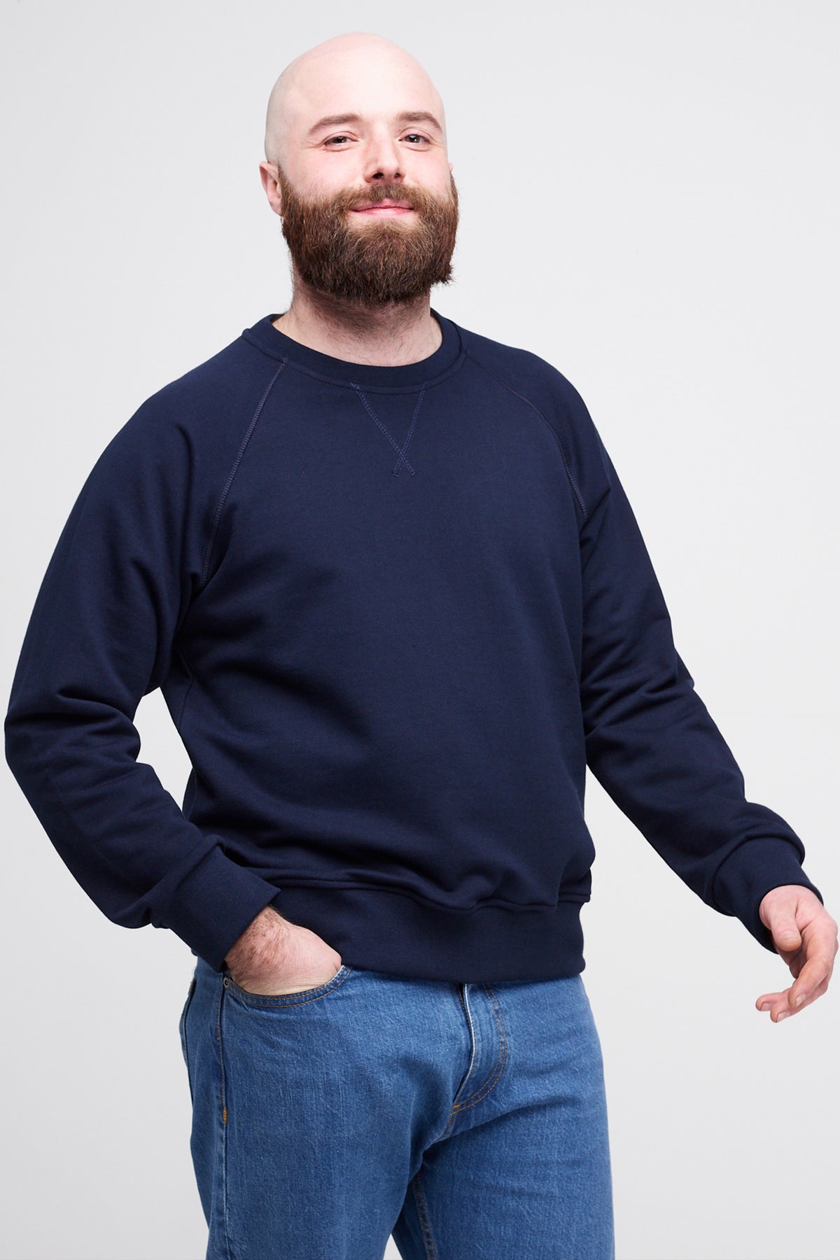 Man wearing a navy blue sweatshirt and blue jeans against a plain background