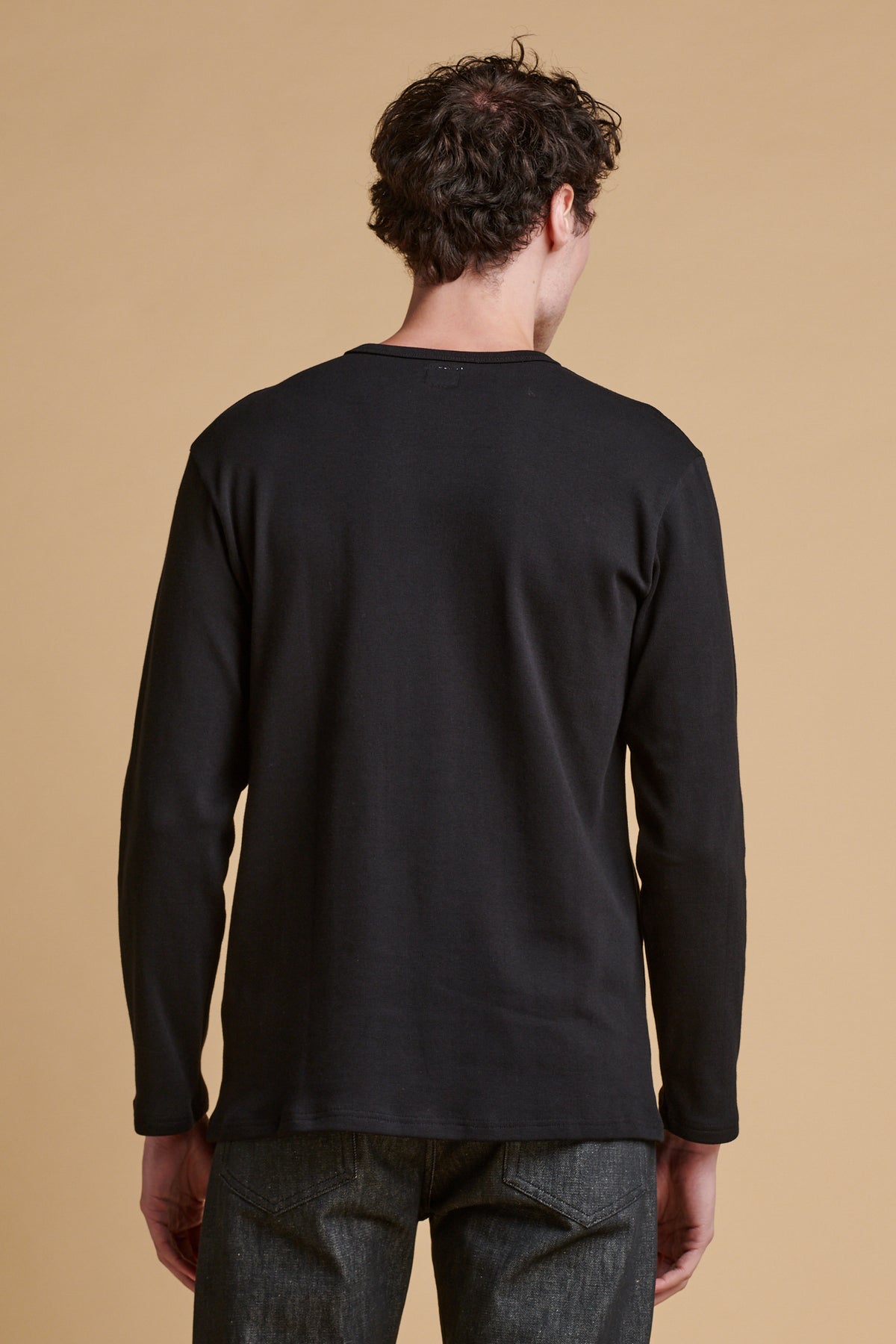 the back of male wearing long sleeve Henley top in black.
