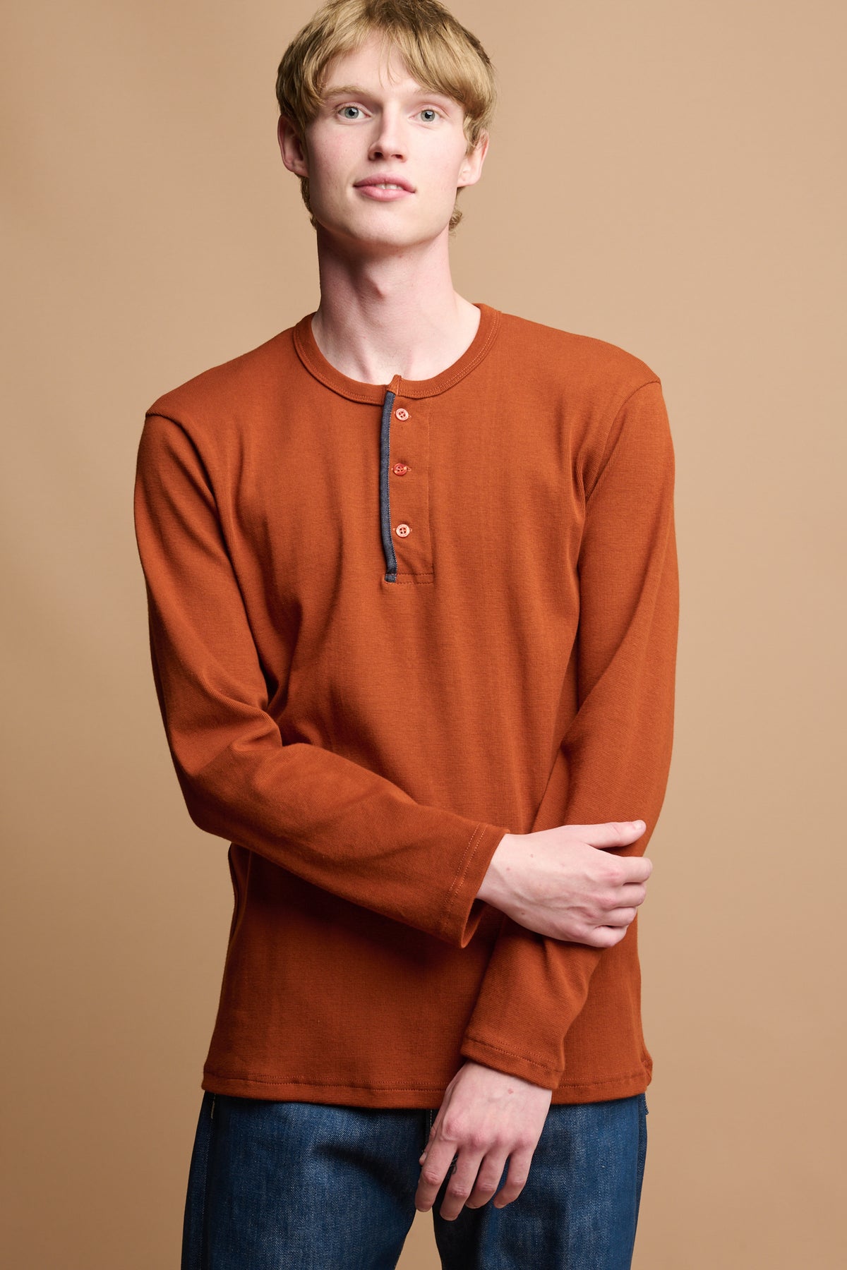 Thigh up of male wearing long sleeve 3 button henley top in cinnamon