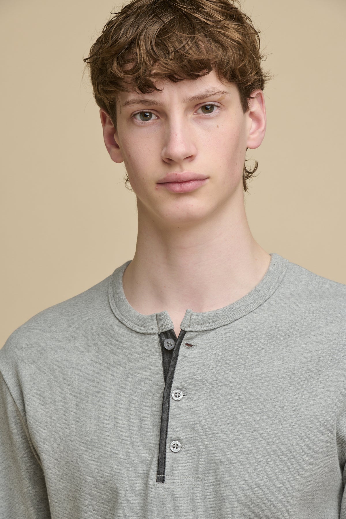Portrait of male wearing long sleeve Henley top in grey marl with 3 button fastening