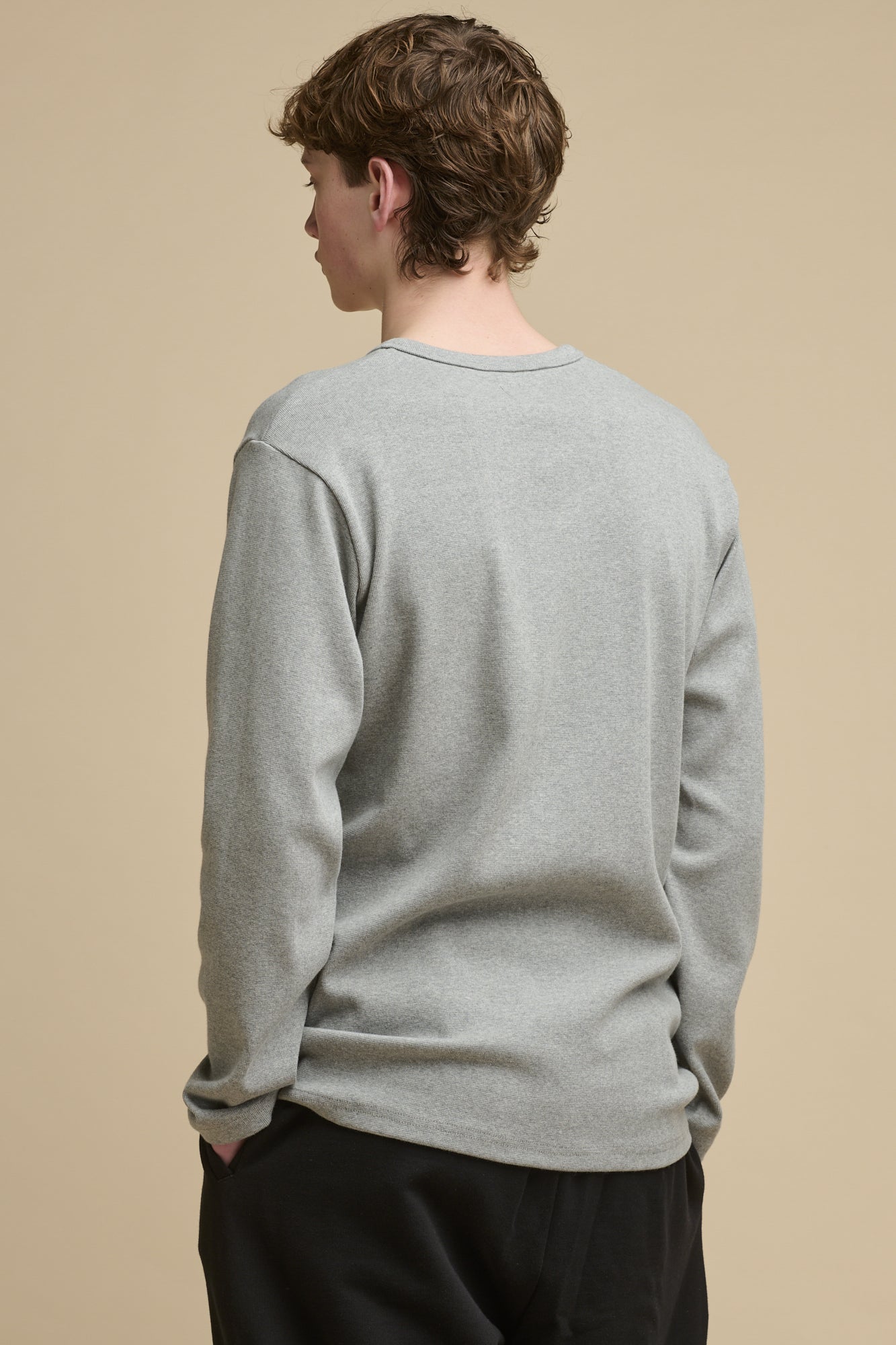 Thigh up front of male wearing long sleeve Henley top in grey marl with his hands in the pockets of black sweatpants