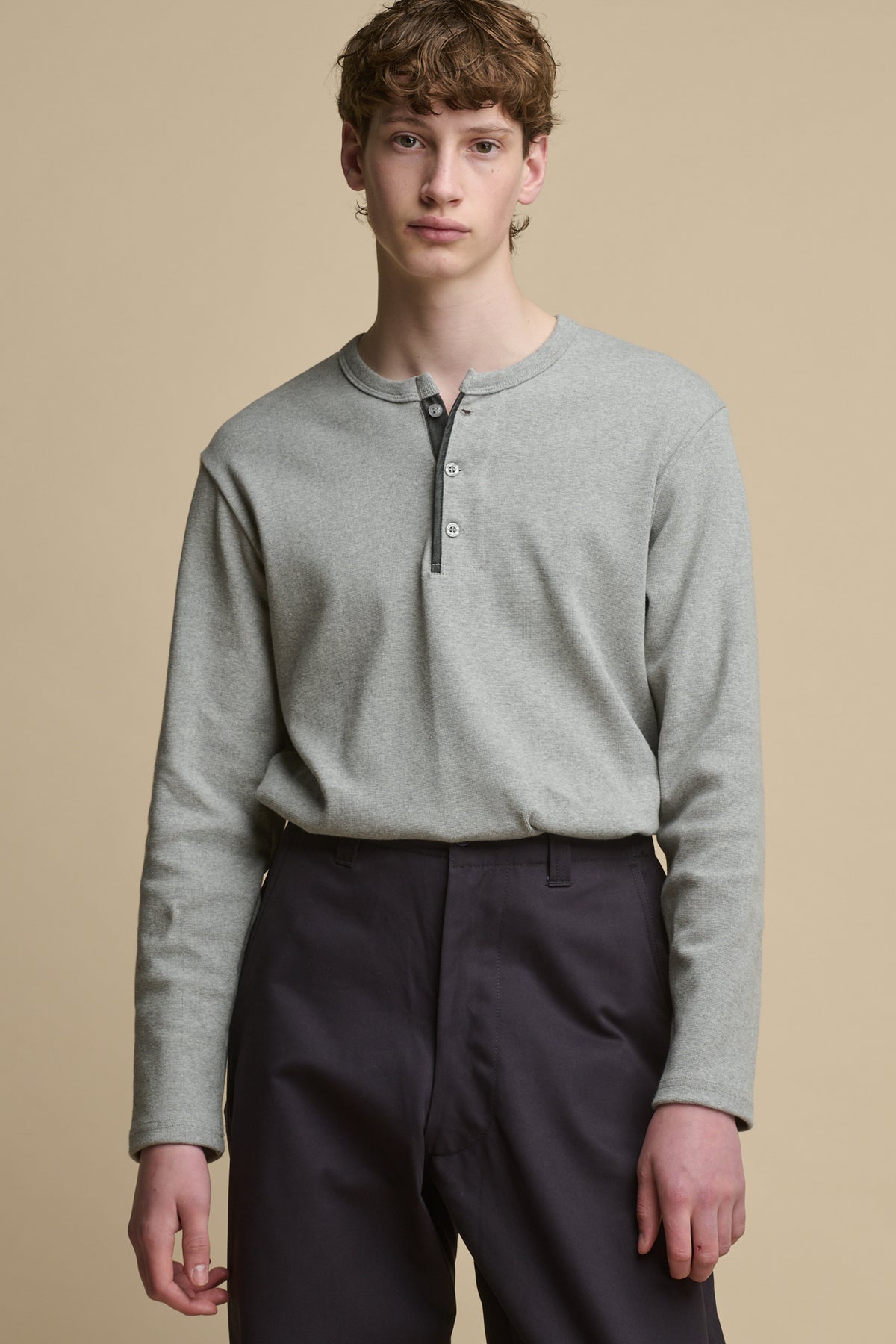 Thigh up image of male wearing long sleeve Henley top in grey marl tucked into field trousers in olive