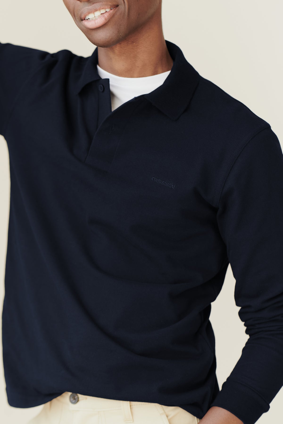 black male wearing an unbuttoned navy community clothing long sleeve polo shirt with a white t-shirt underneath