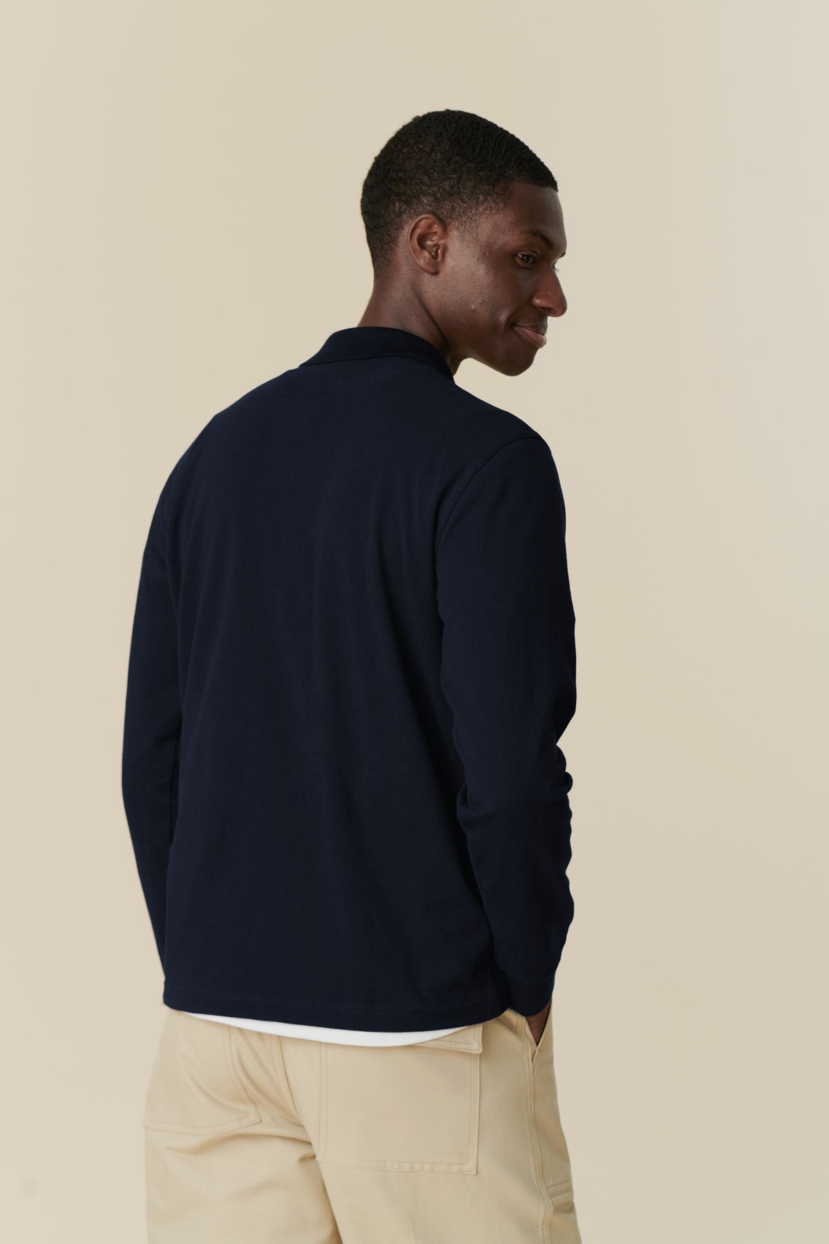 back angle image of black male wearing long sleeve community clothing polo shirt in navy with the combat trouser in putty
