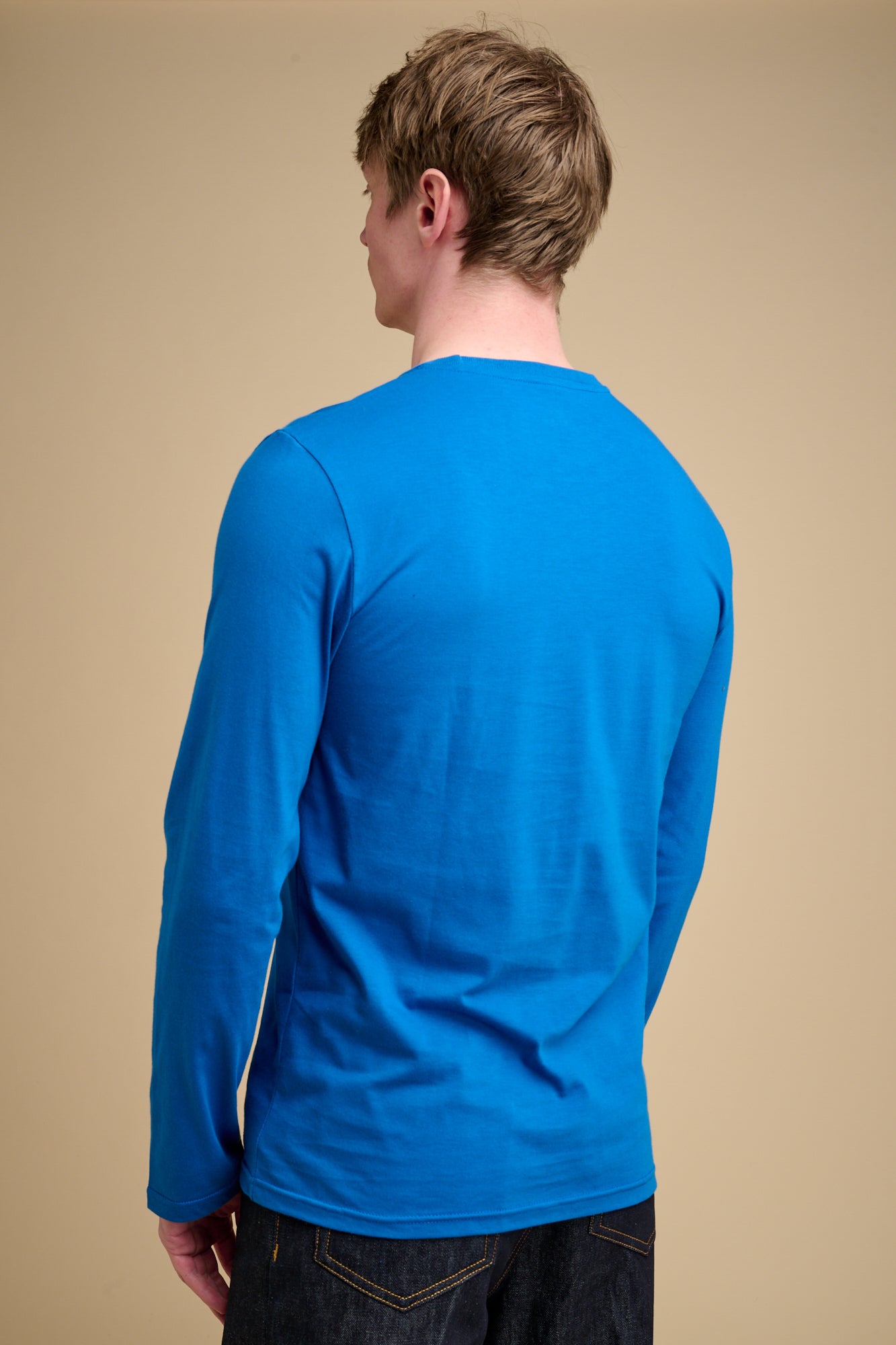 Man wearing a cobalt blue long-sleeve t-shirt against a beige background.