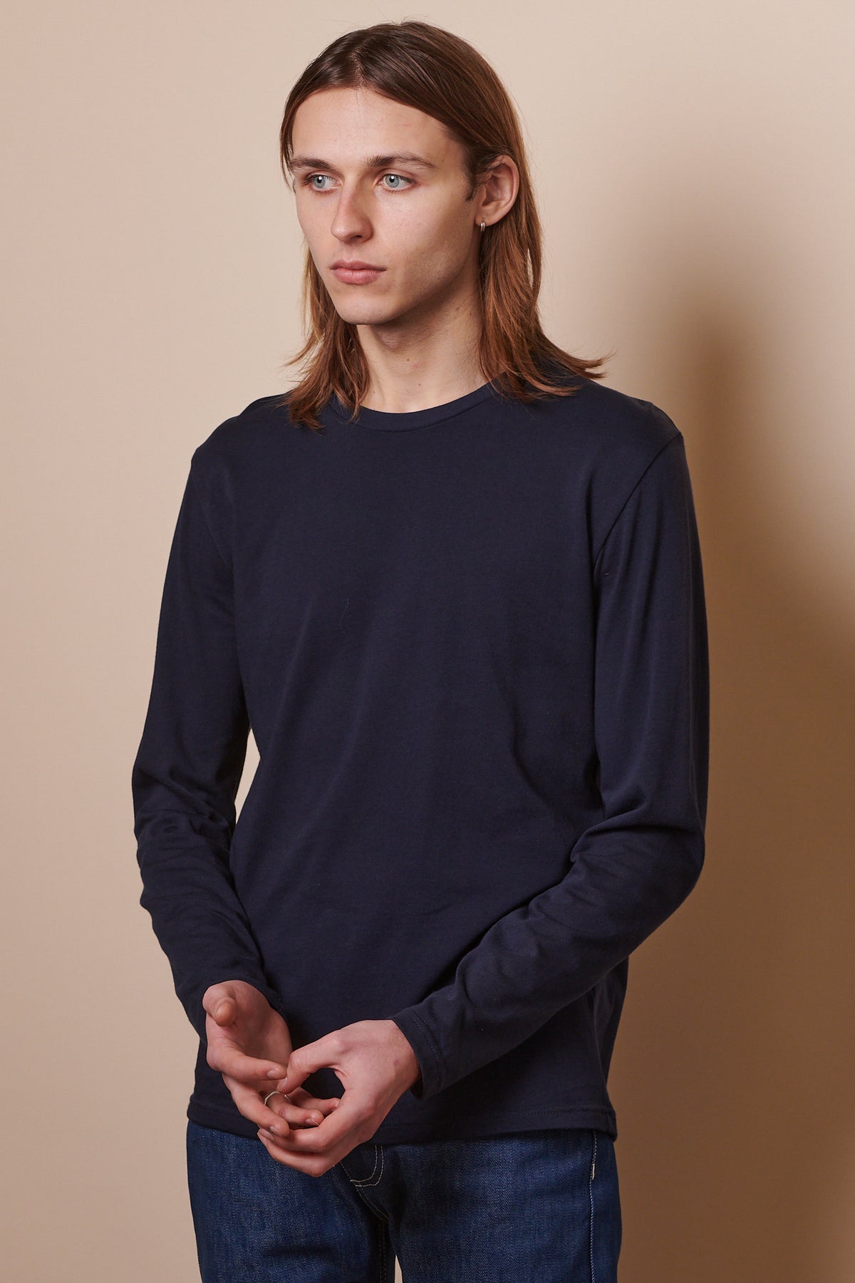 
            Thigh up image of male with shoulder length brown hair wearing wearing long sleeve crew neck t shirt in navy, paired with blue jeans.