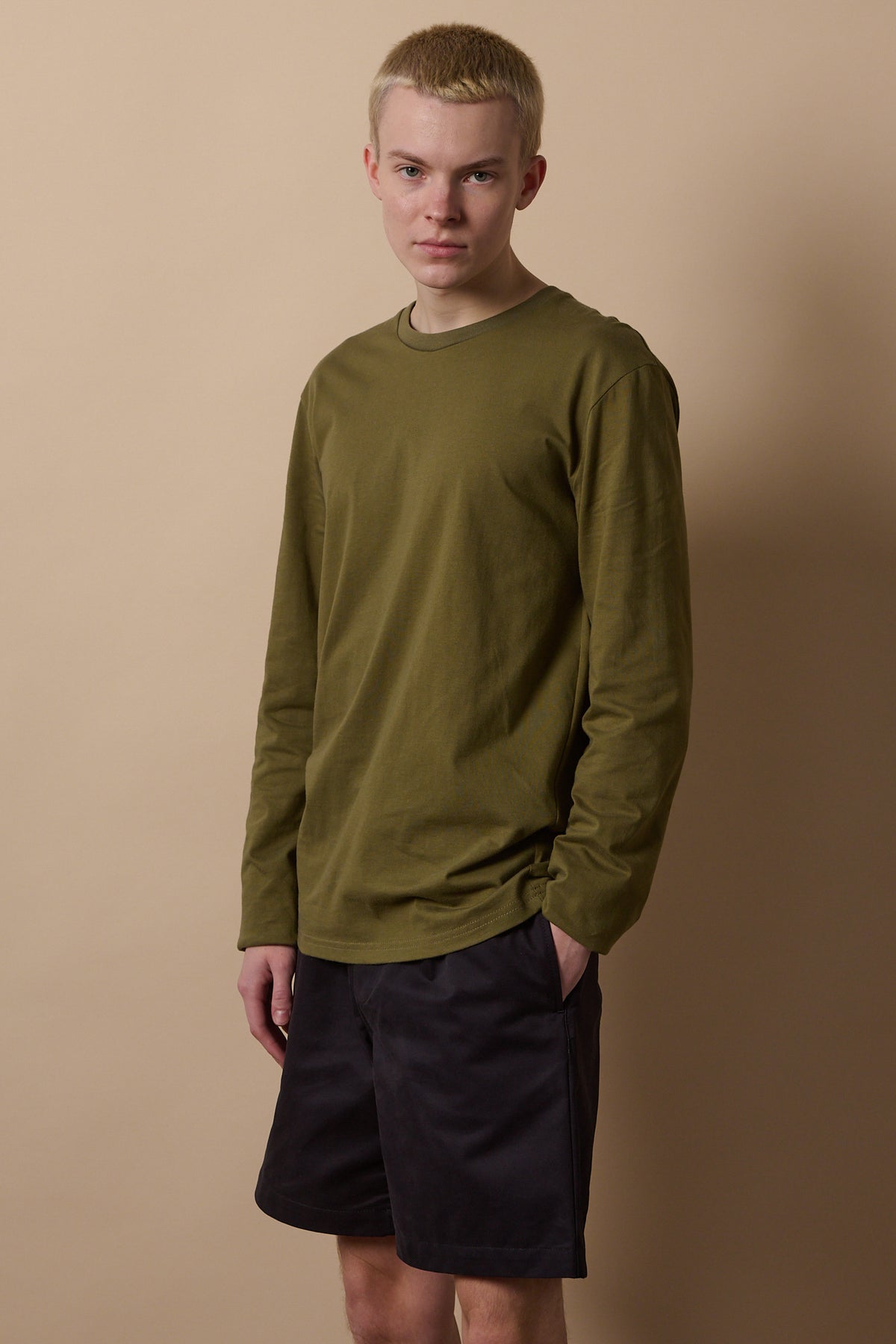 Knee up image of male wearing long sleeve t shirt in olive paired with navy shorts