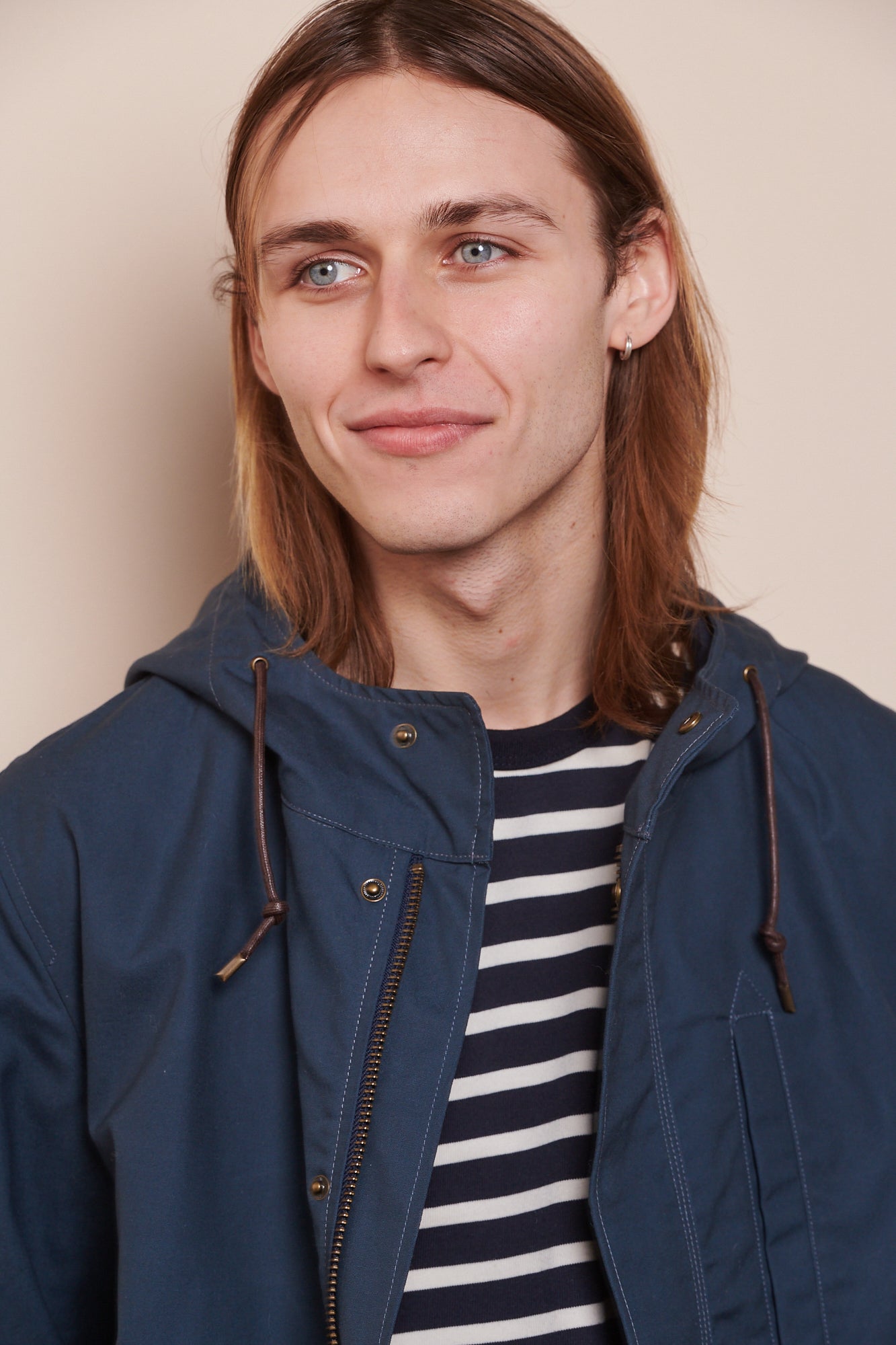 Thigh up image of male wearing mountain parka in navy holding hands behind his back, making two large front pockets visible