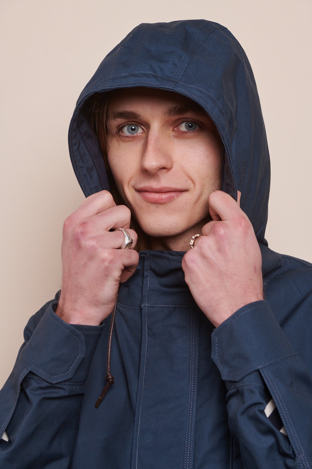 Portrait of male wearing hood up of mountain parka holding front of hood, showing adjustable cuff of sleeve straps