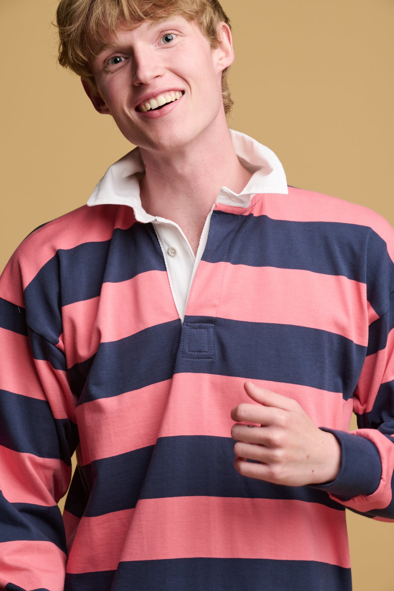 Waist up image of male wearing rugby shirt in navy/ cerise stripe with unbuttoned white collar