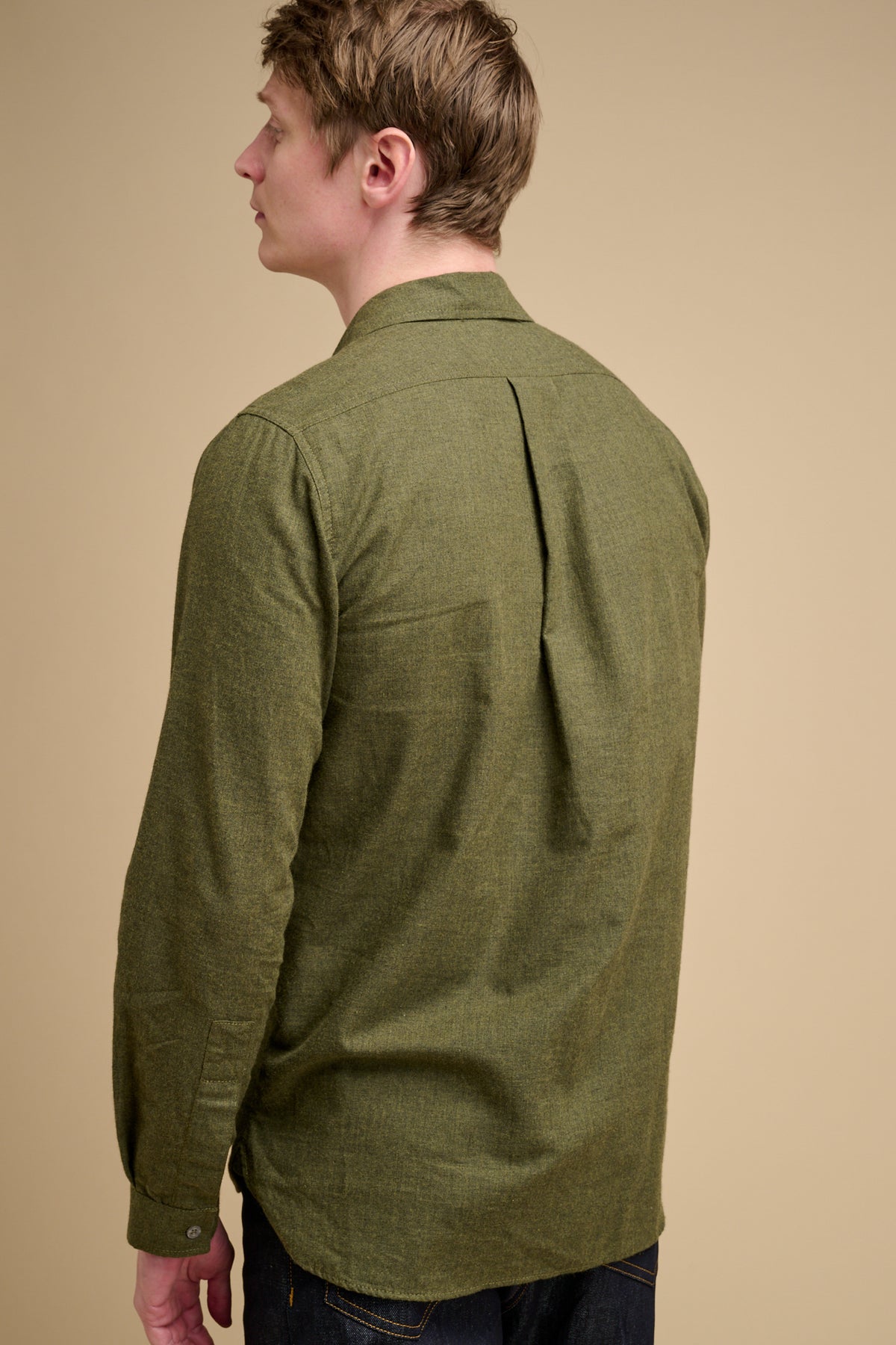 The back of man wearing an olive green brushed cotton shirt against a beige background.