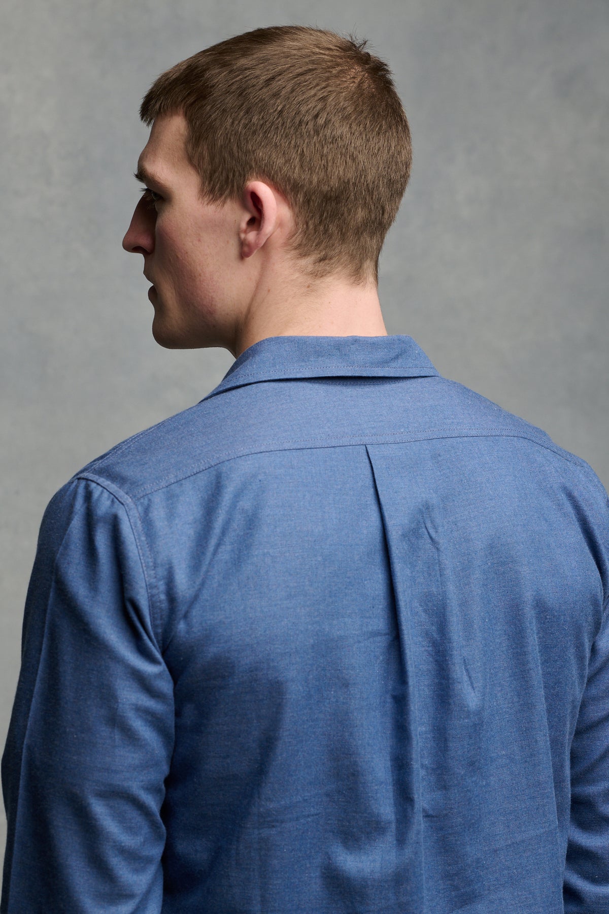 
            Close up of the back of white, brunet male wearing Oli shirt in RAF blue with pleat detail on the back of shoulders
