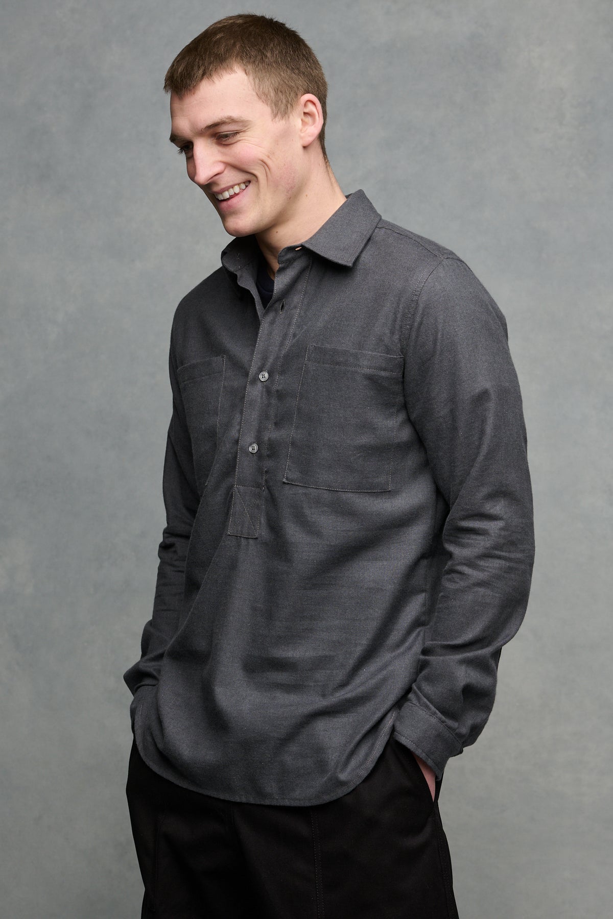 
            Thigh up image of smiley male wearing Oli shirt in slate with hands in pockets of cameraman pants in black