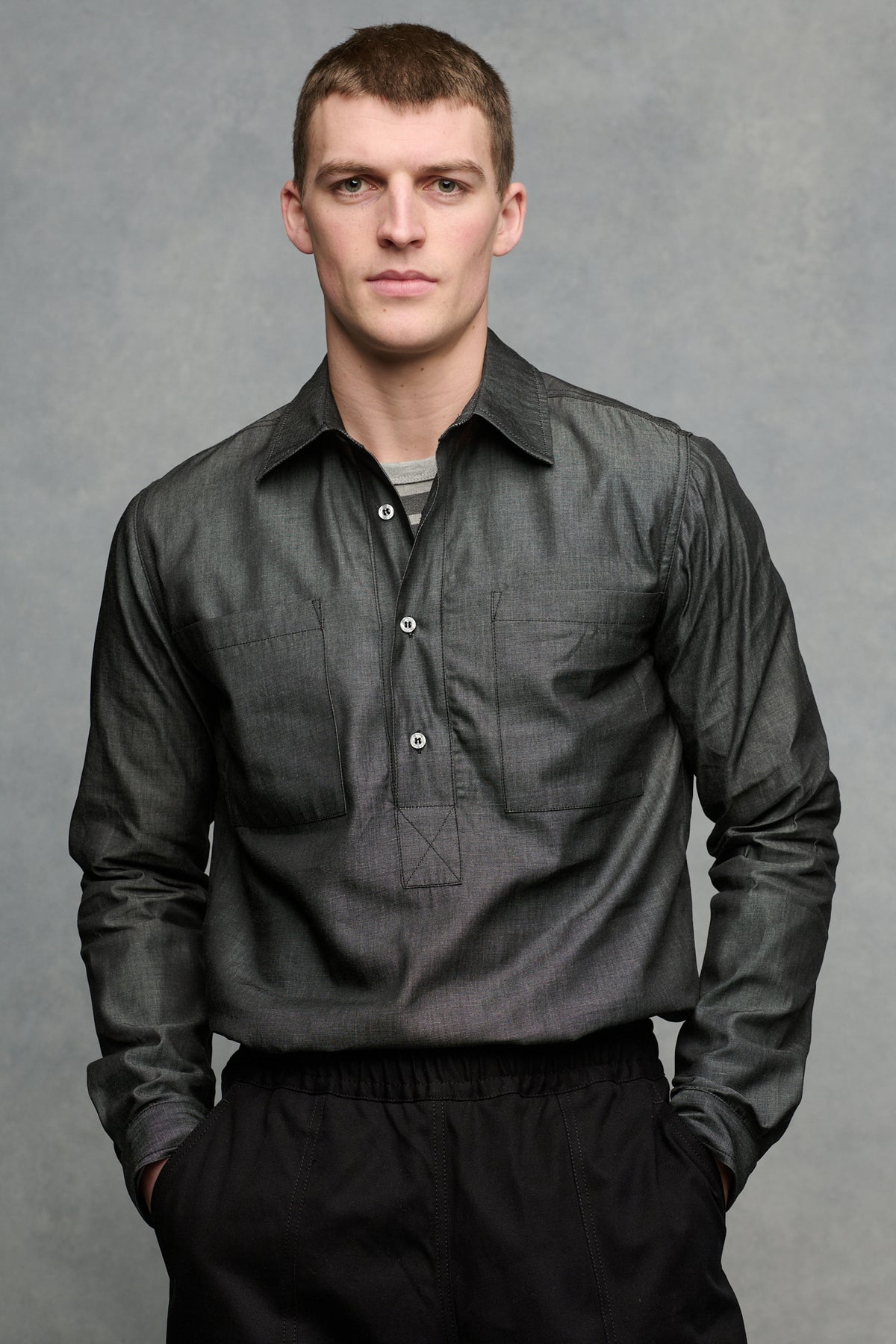 Thigh up front of male wearing Oli half placket lightweight denim shirt in black tucked into cameraman pants in black