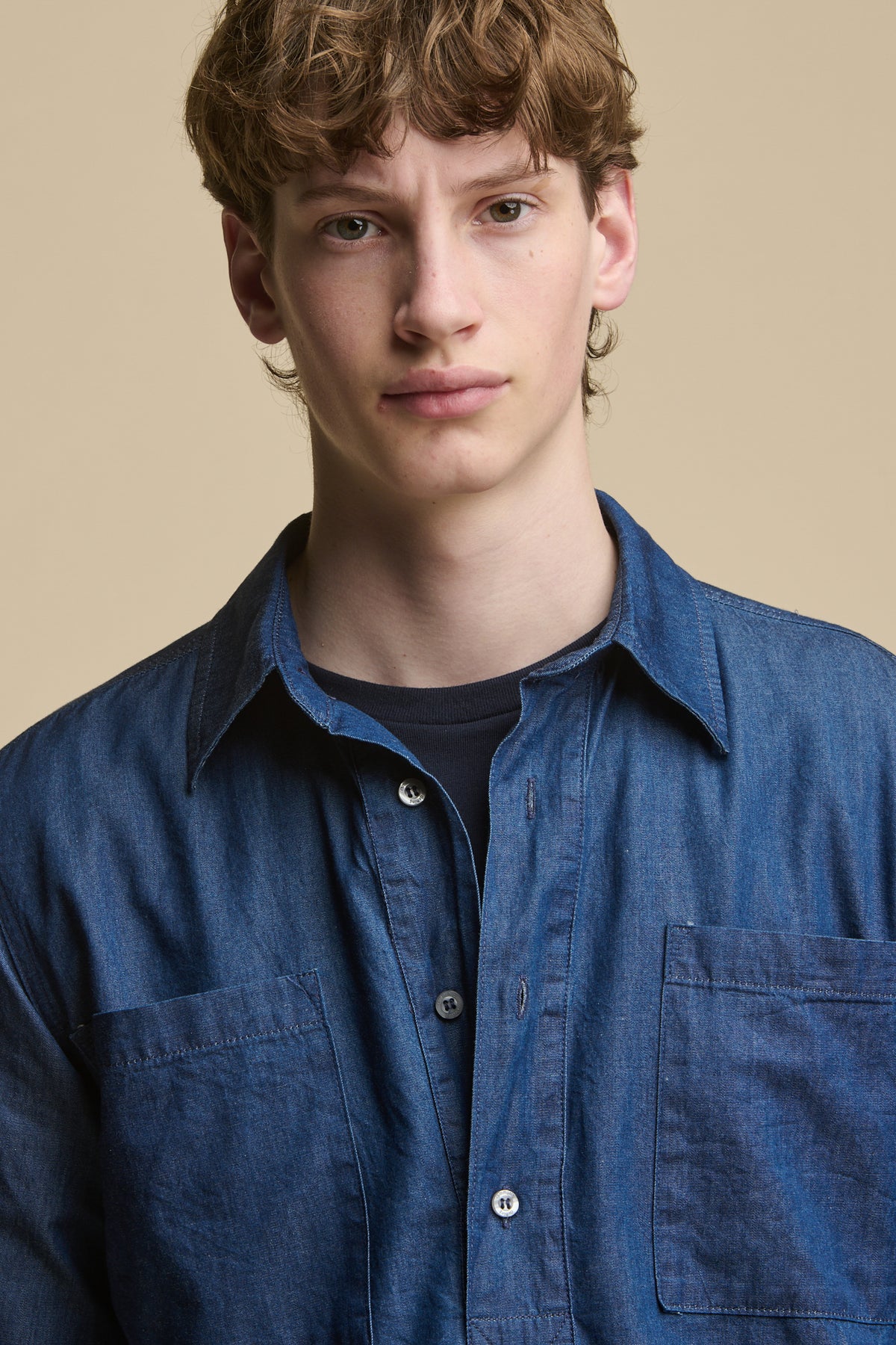 
            Portrait of male showing the half placket detail and front pockets of men&#39;s half placket lightweight denim shirt worn over navy short sleeve t shirt