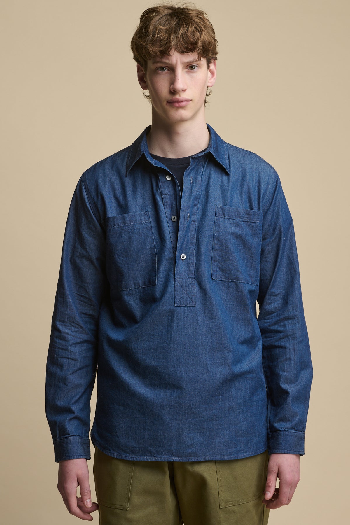 Thigh up image of male white wearing Oli Half Placket Lightweight Denim Shirt in Indigo worn over short sleeve t shirt in navy