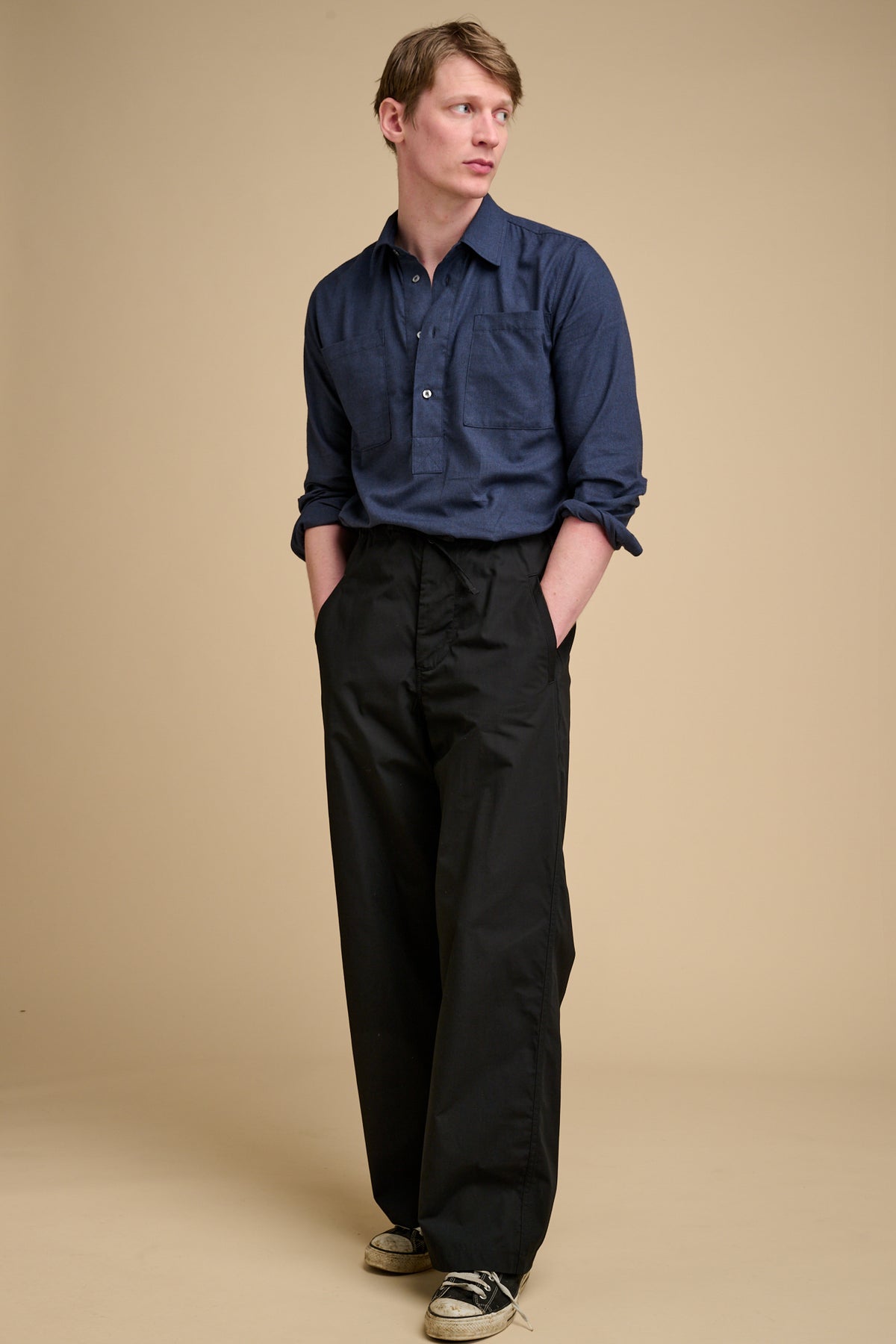 Man wearing a blue shirt and black pants against a beige background
