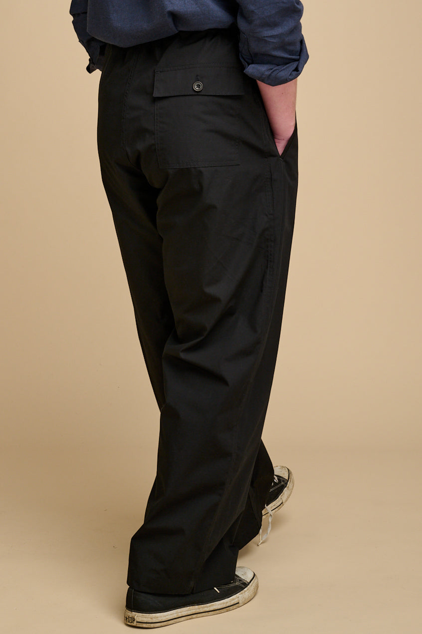 The back of man wearing black trousers on a beige background.