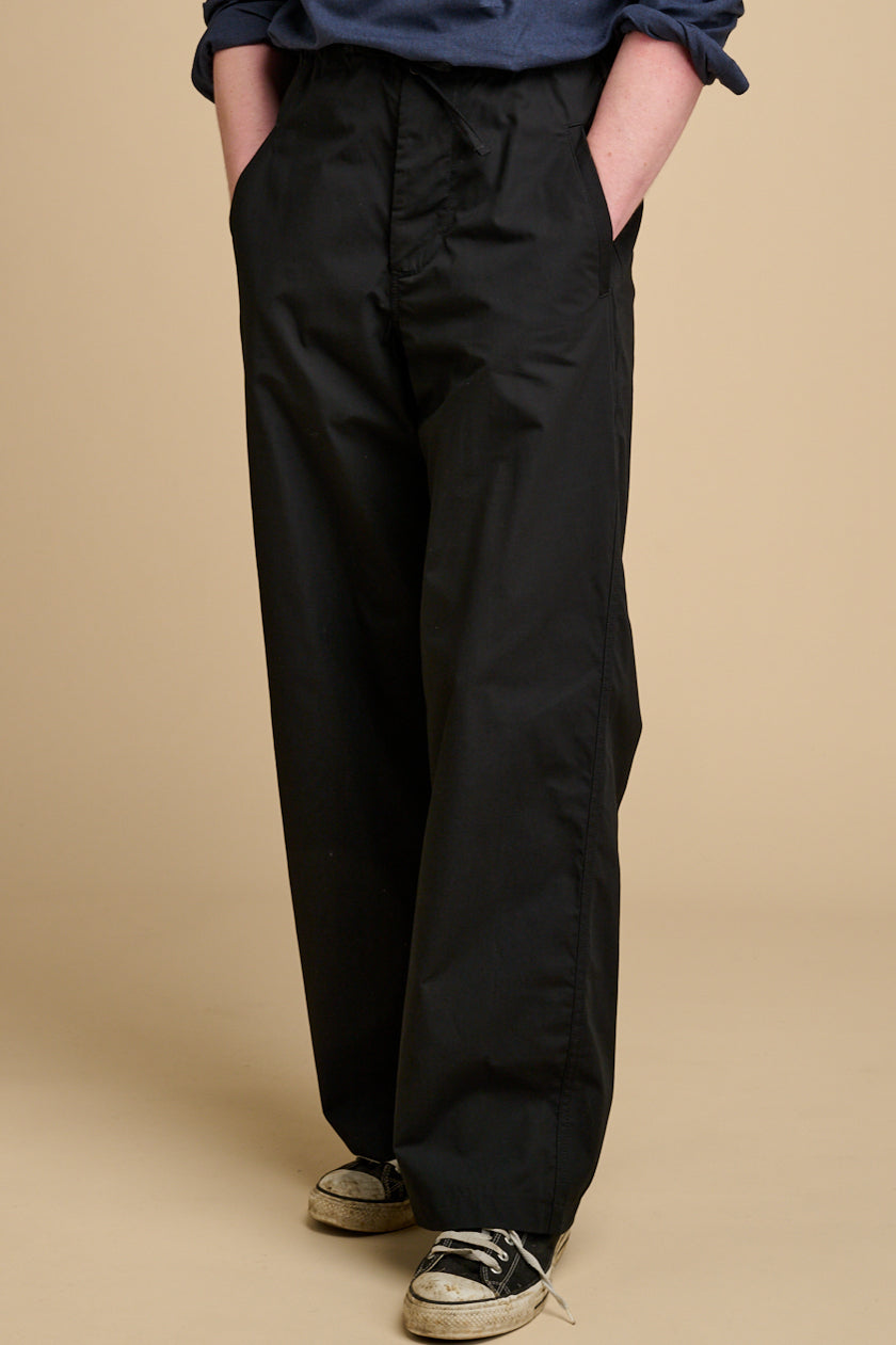 Man wearing black pants and a blue shirt on a beige background.