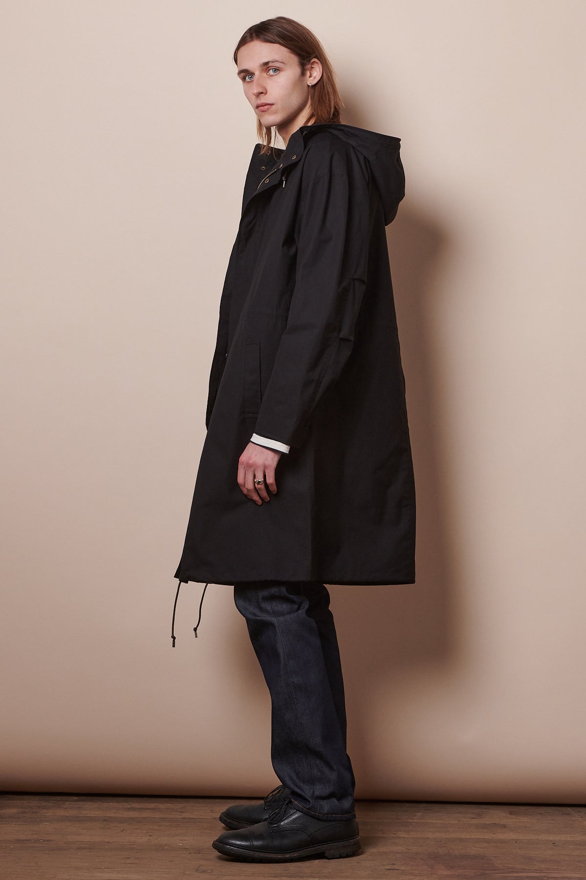 Side of male wearing parka in black, adjustable hem drawcord.