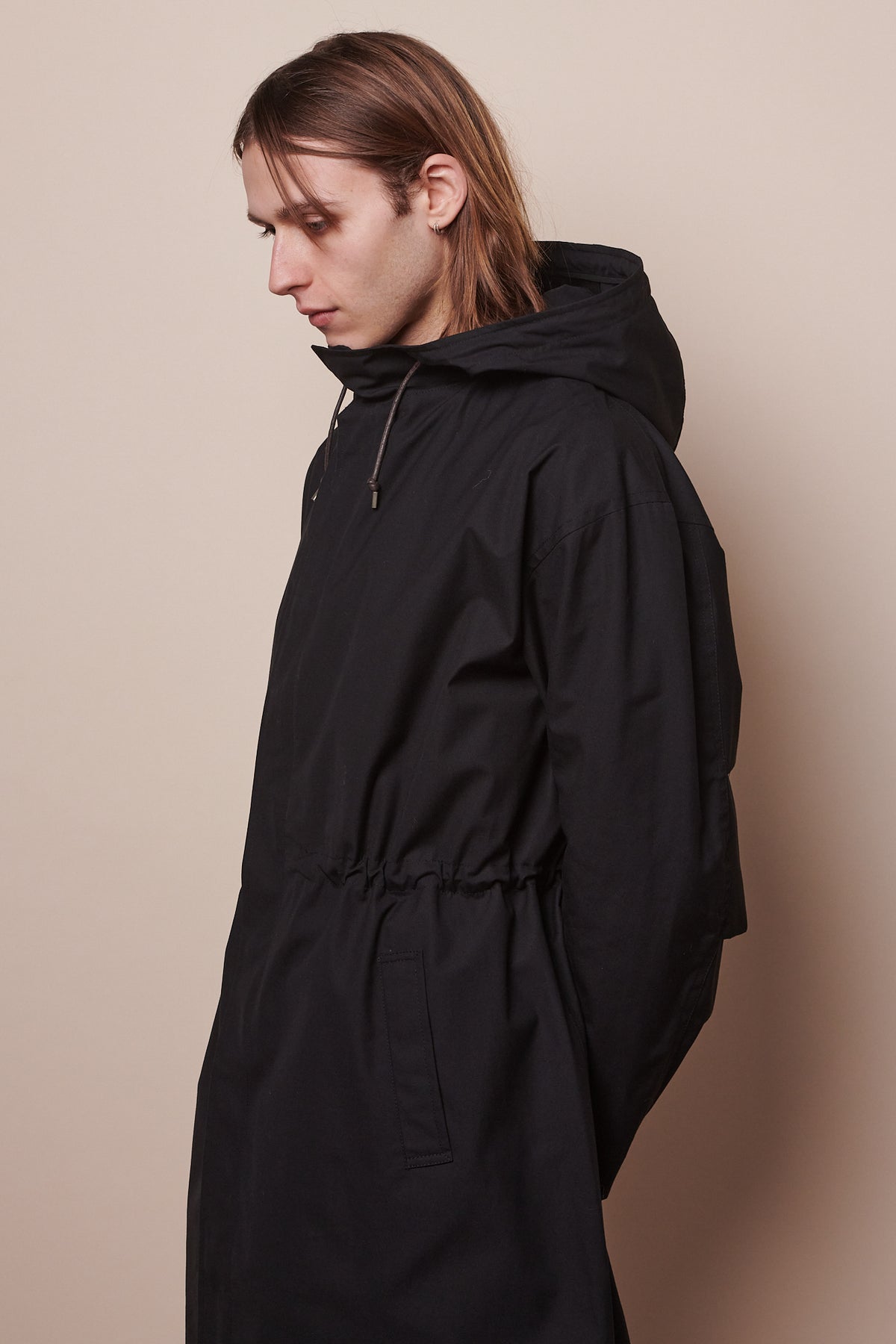 Thigh up image of male wearing zipped parka in black with waist synched in slightly with drawcord