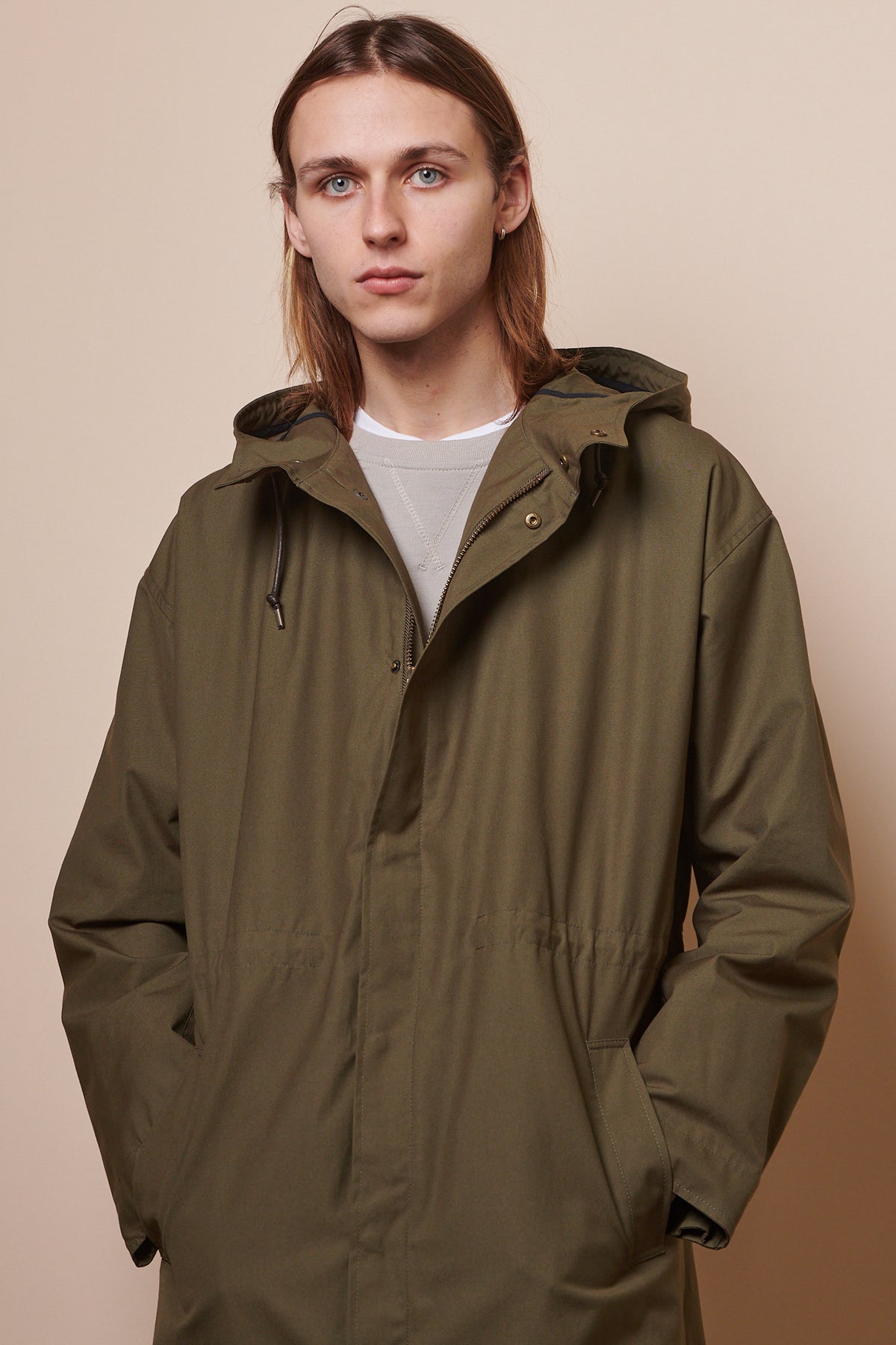 Thigh up image of male wearing parka in olive with hands in front pockets