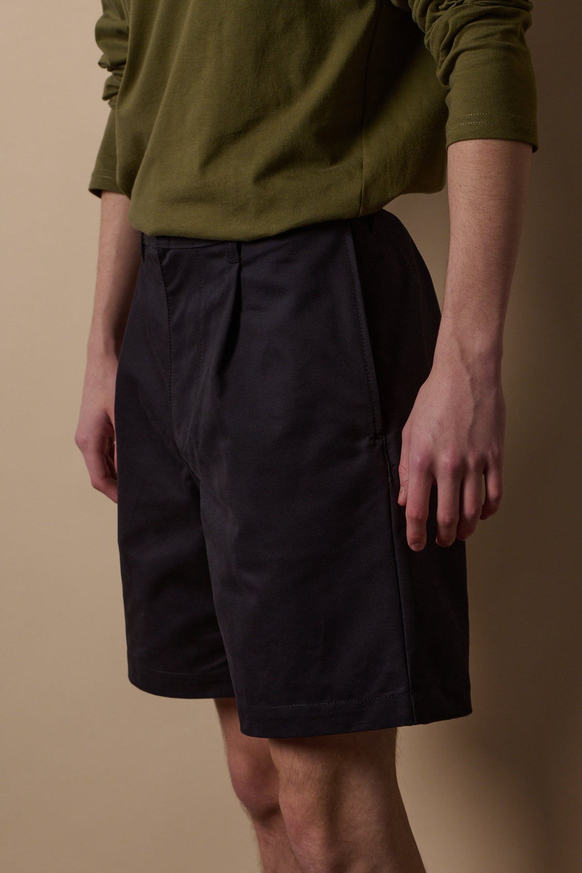 
            Front of pleated shorts in navy with olive t shirt tucked in