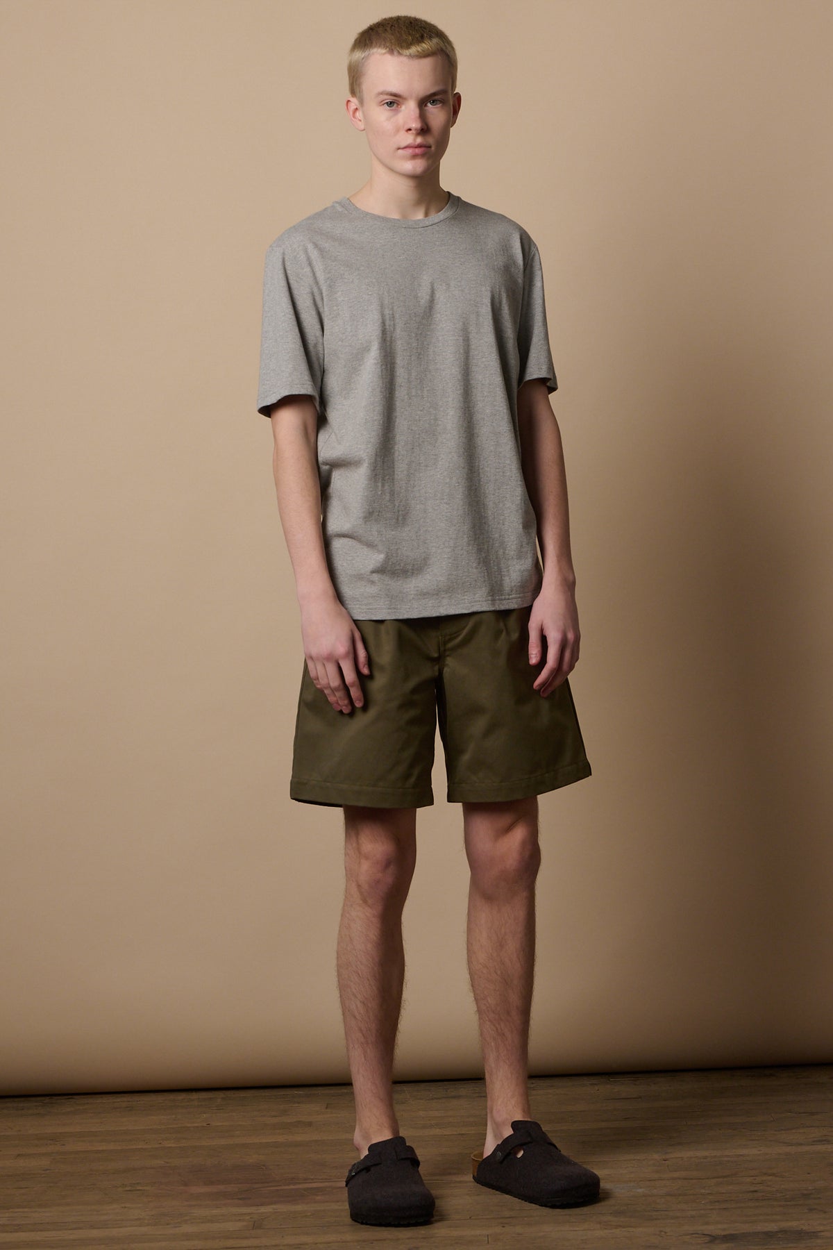 Full body image of male wearing pleated shorts in olive with short sleeve t shirt