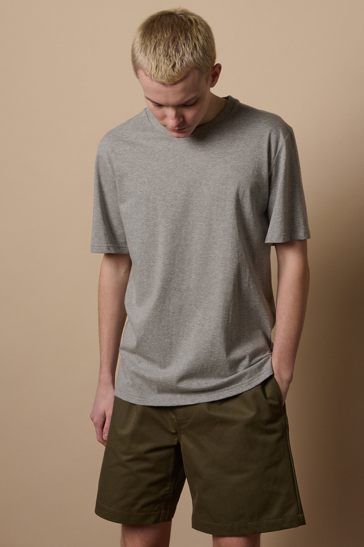 Knee up image of white make wearing pleated shorts in olive paired with short sleeve grey t shirt