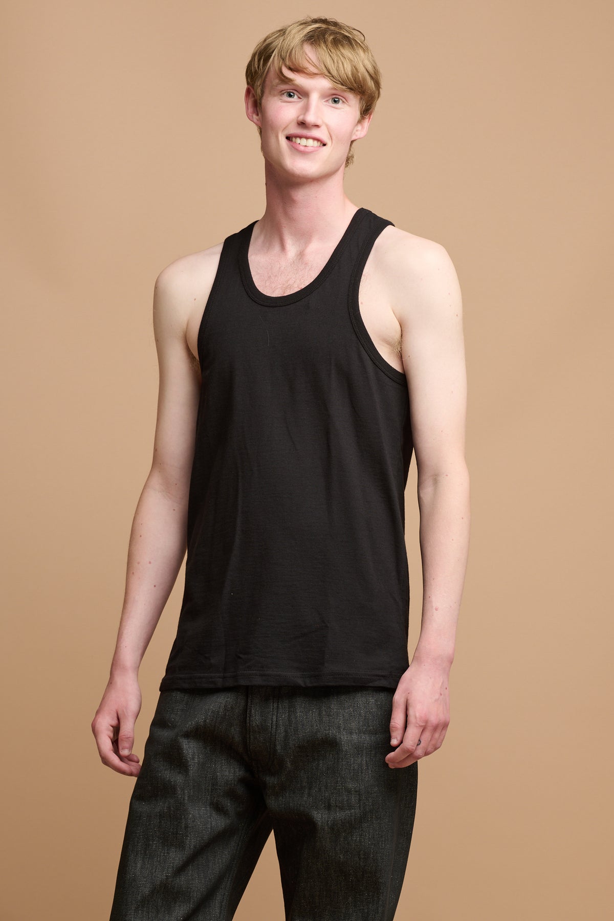 
            Thigh up image of male wearing plastic free racer back vest in black paired with loose fit button fly arran jean in black