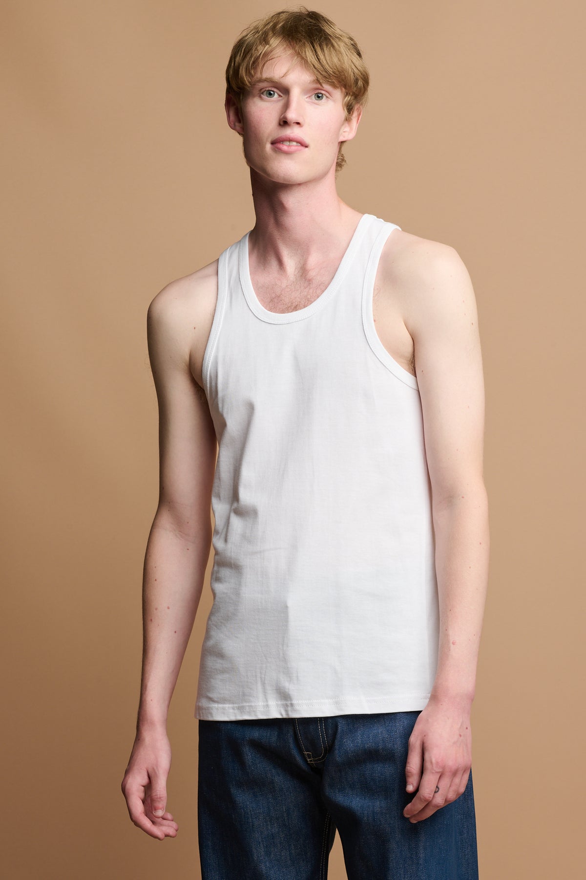 
            White male wearing plastic free racer back vest in white paired with blue jeans for everyday wear