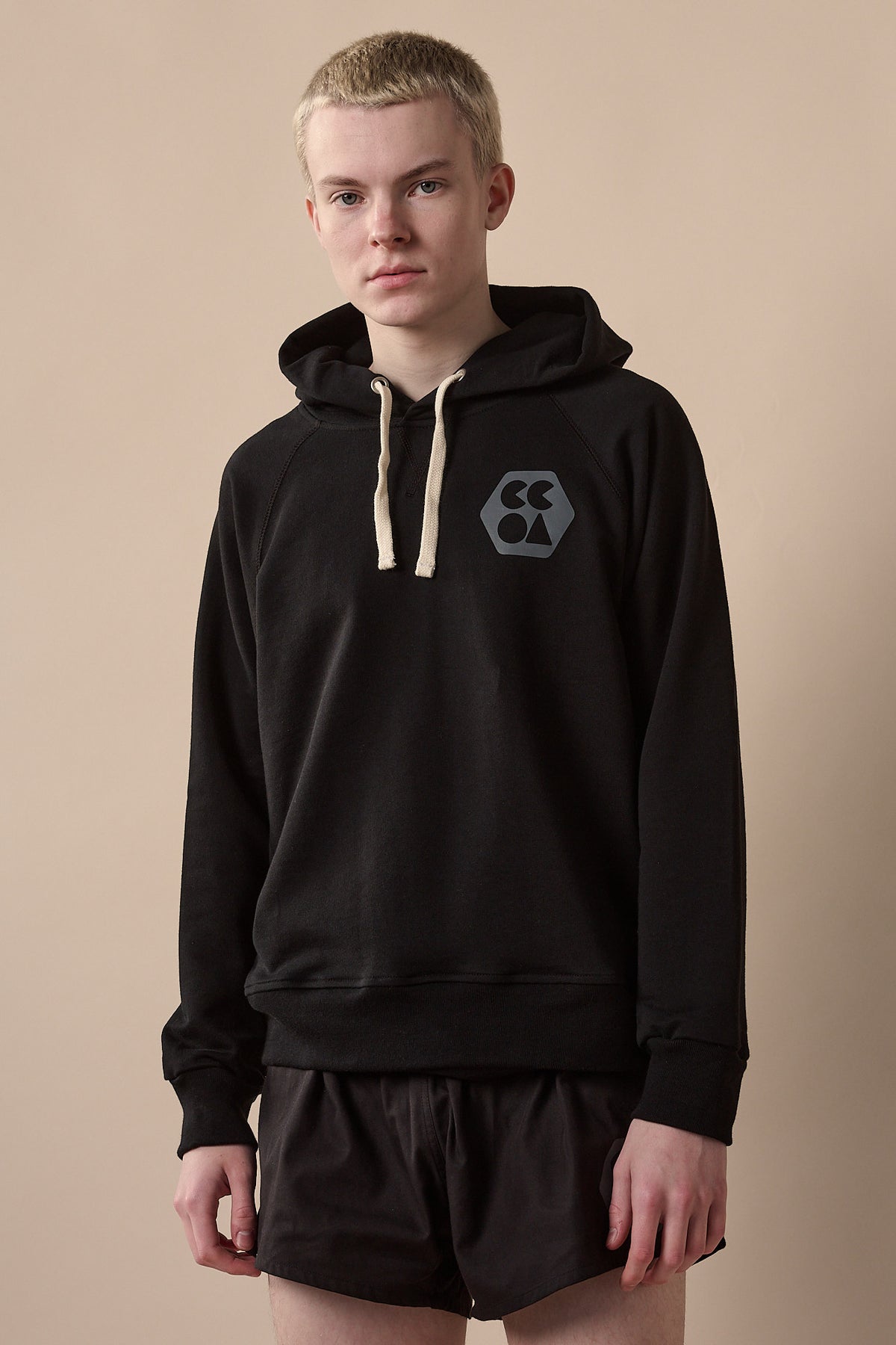 Thigh up image of white male wearing men's raglan hooded sweatshirt plastic free in black with CCOA logo