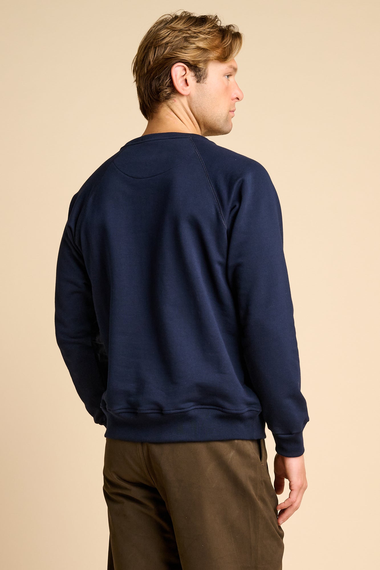 Man wearing a navy blue sweatshirt against a beige background.
