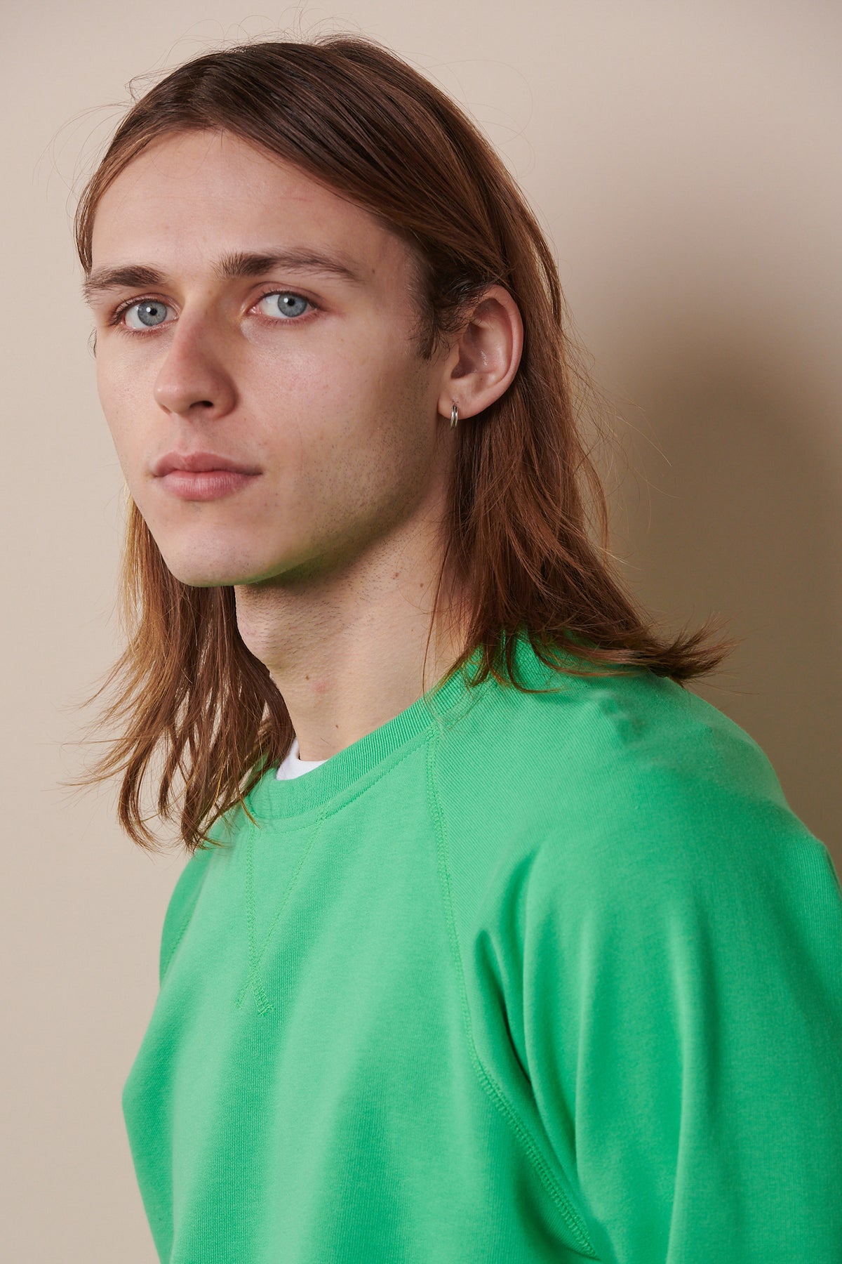 Portrait of white male with shoulder length brown hair wearing raglan sweatshirt in apple green
