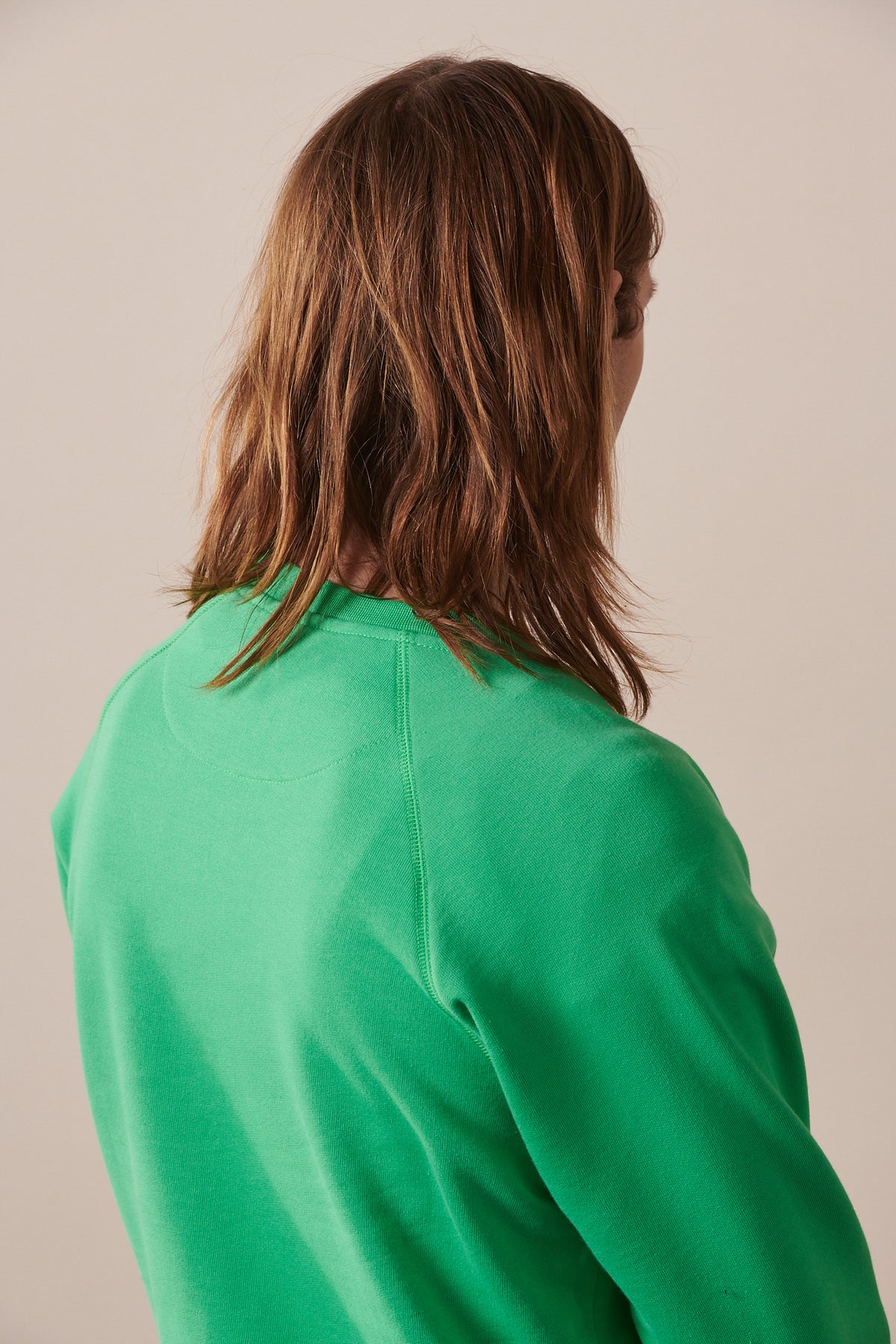 Back of male with shoulder length hair wearing raglan sweatshirt in apple green