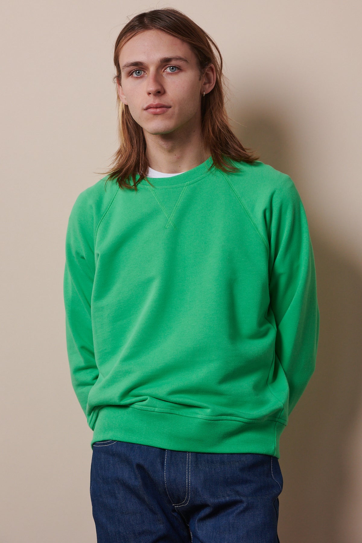 Thigh up image of male wearing raglan sweatshirt in apple green with hands held behind back, paired with blue jeans