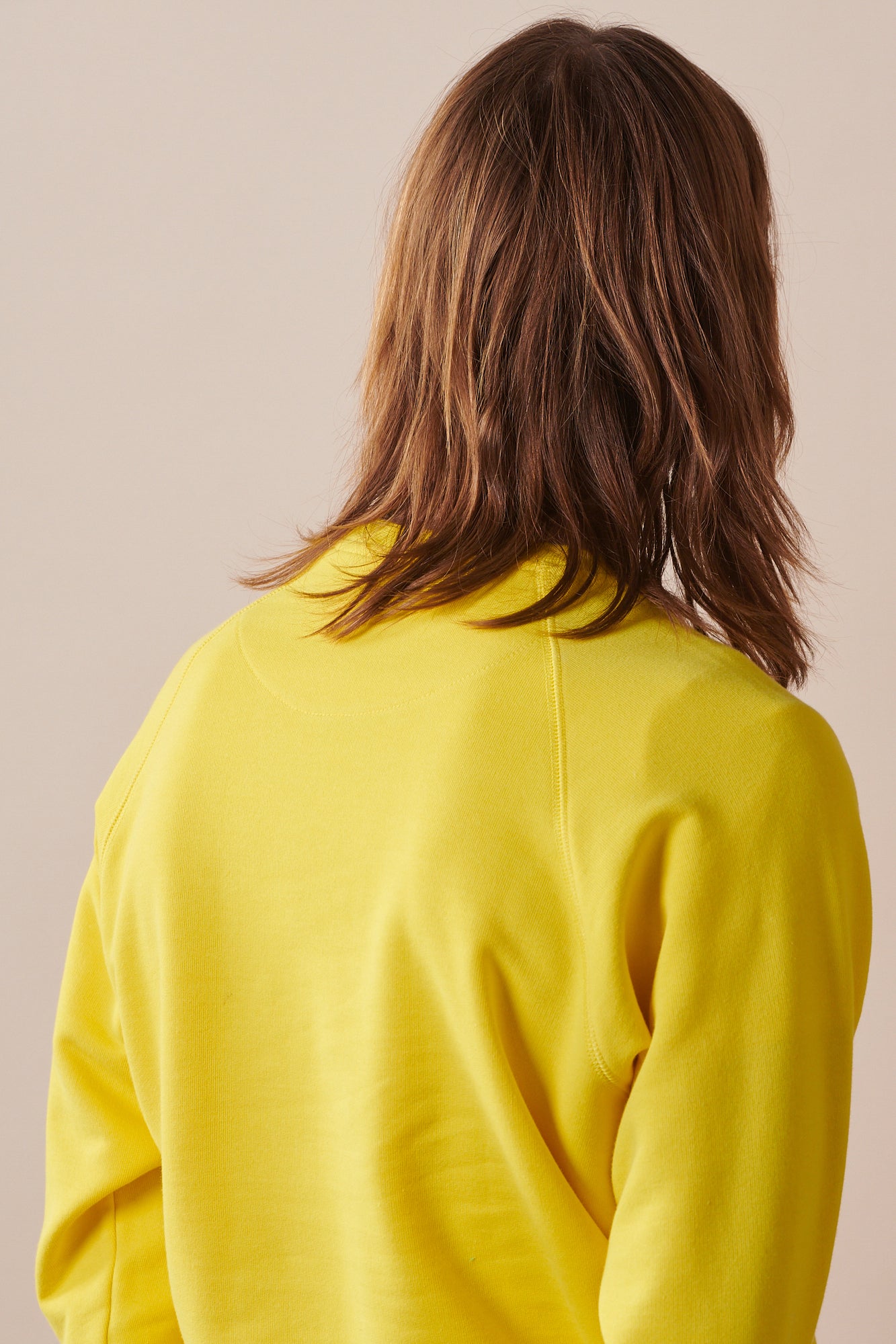 Male with shoulder length brown hair wearing raglan sweatshirt in canary yellow paired with blue jeans.