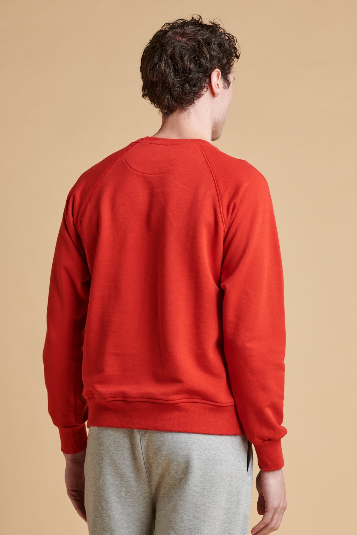 Thigh up of the back of male wearing raglan sweatshirt in crimson.