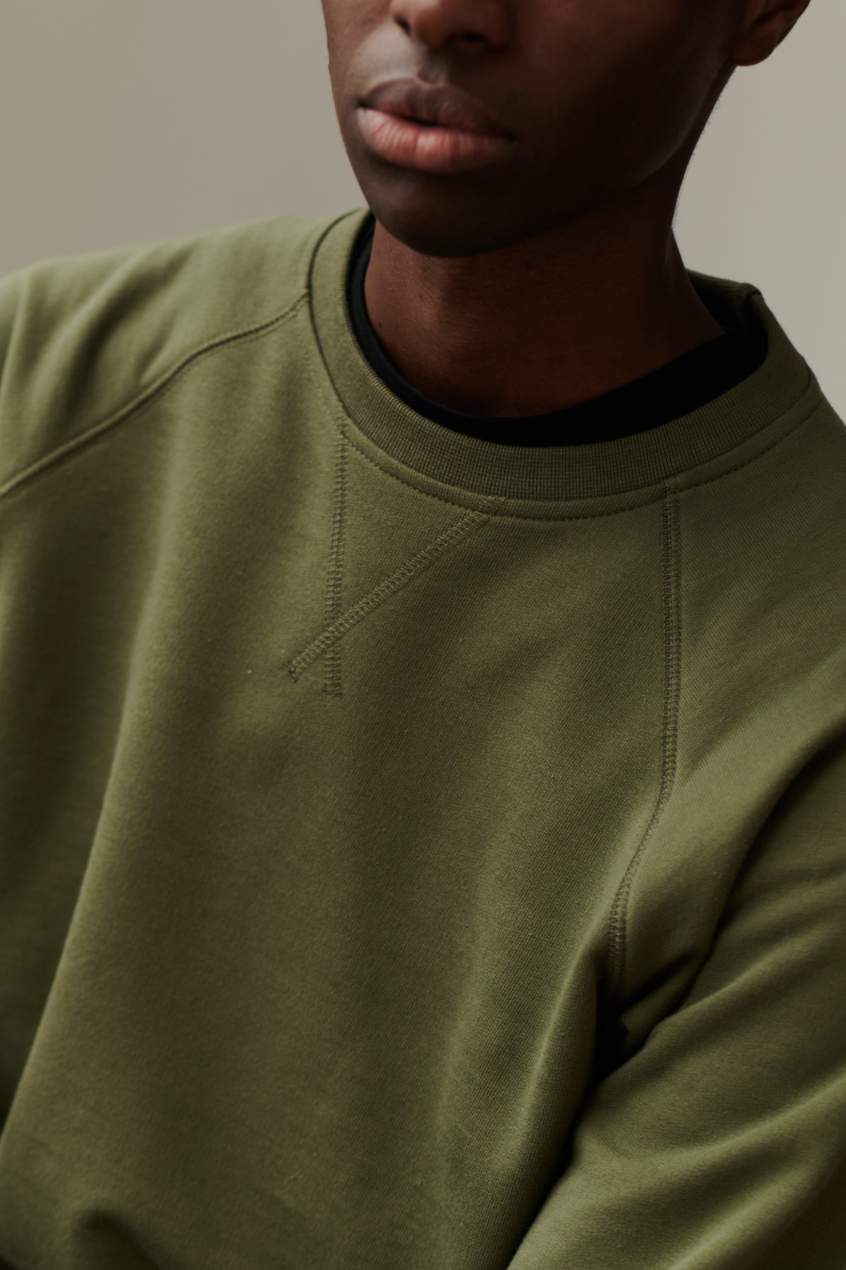 Crew neck detail of male wearing raglan sweatshirt in olive