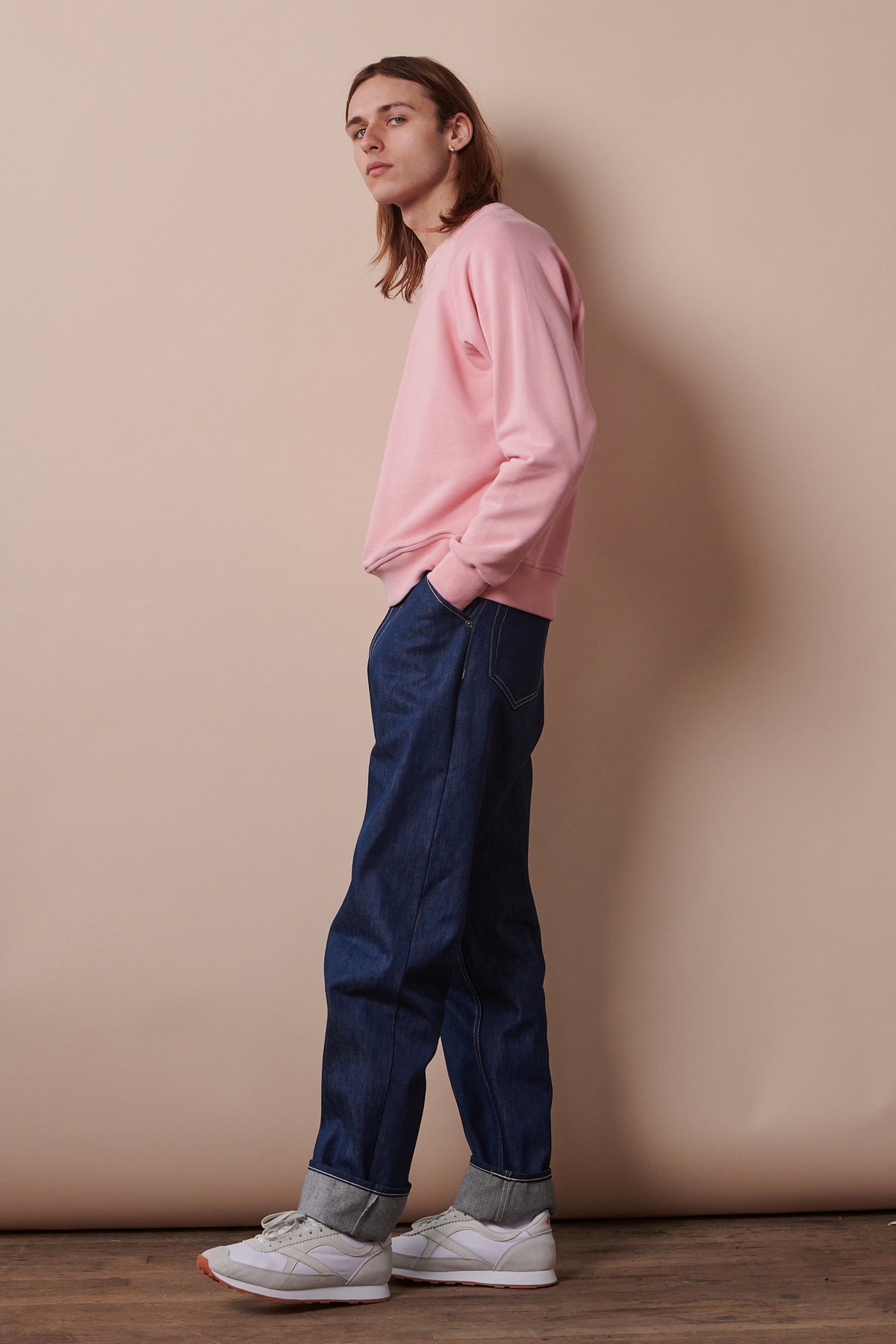 
            Full body image of the side of male wearing raglan sweatshirt in pale pink paired with chore jeans in blue