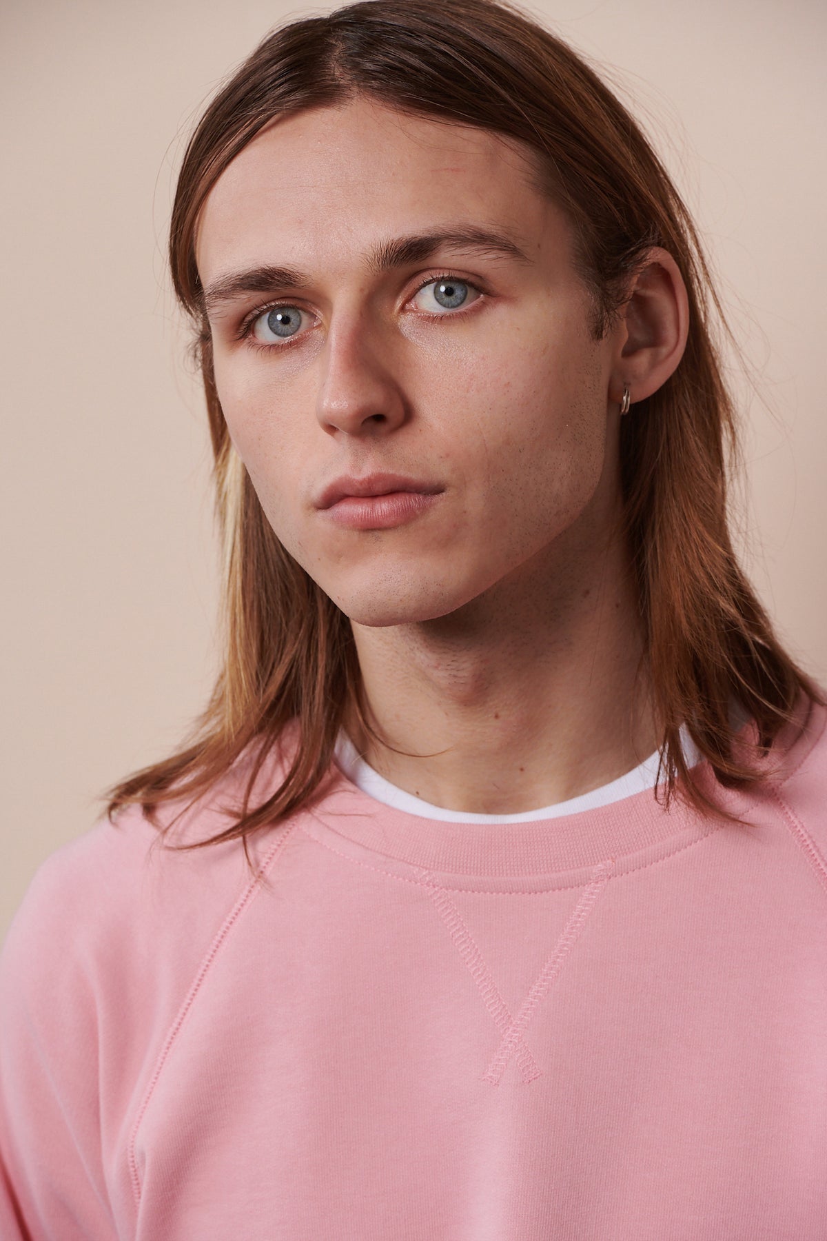 
            Portrait of male wearing raglan sweatshirt in pale pink layered over crew neck white t shirt.