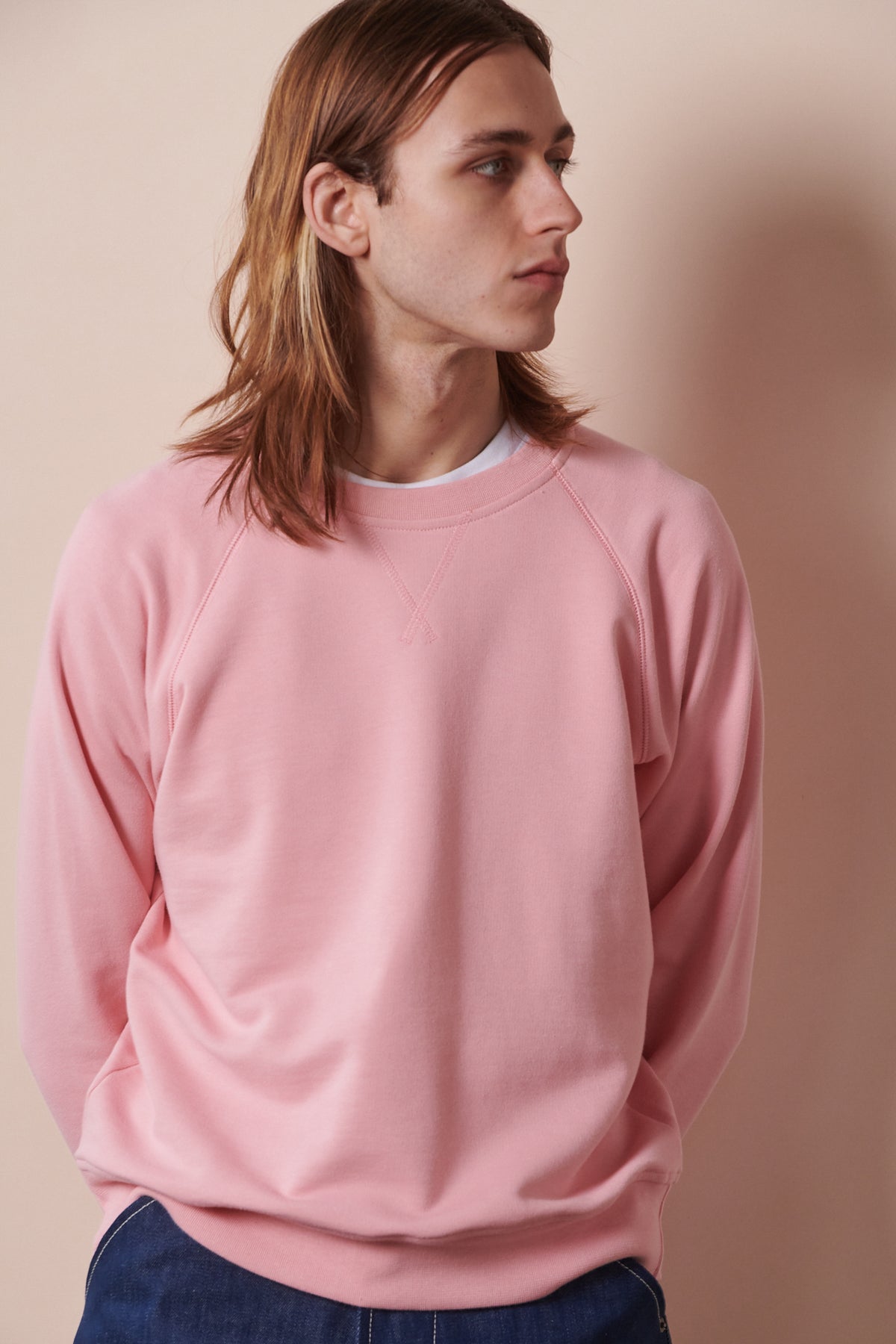 
            Thigh up image of front of male looking towards the side wearing raglan sweatshirt in pale pink layered over white crew neck t shirt