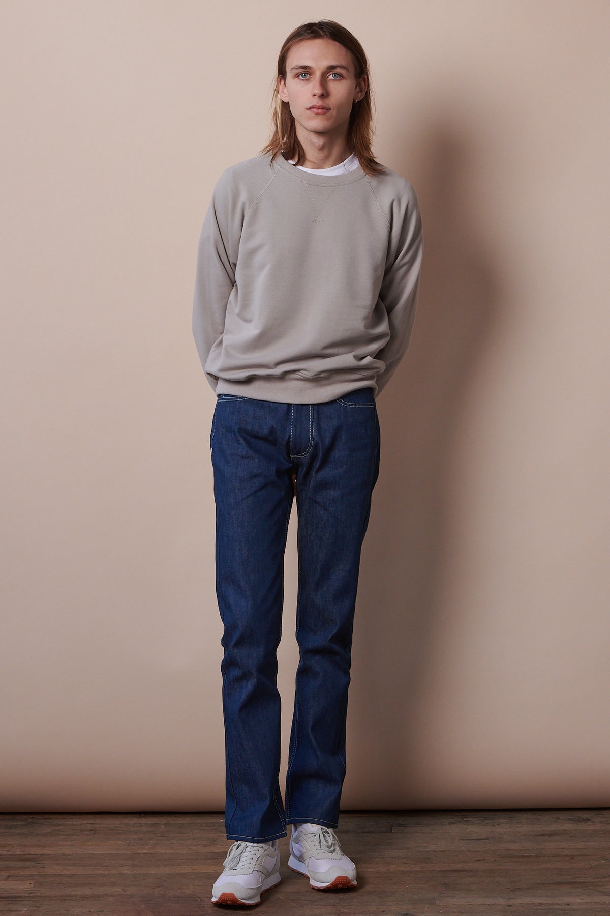 Full body image of male wearing raglan sweatshirt in stone paired with straight cut jeans in blue