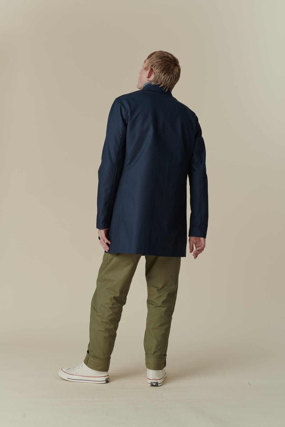Full body image from behind of male wearing mid thigh length raincoat in navy