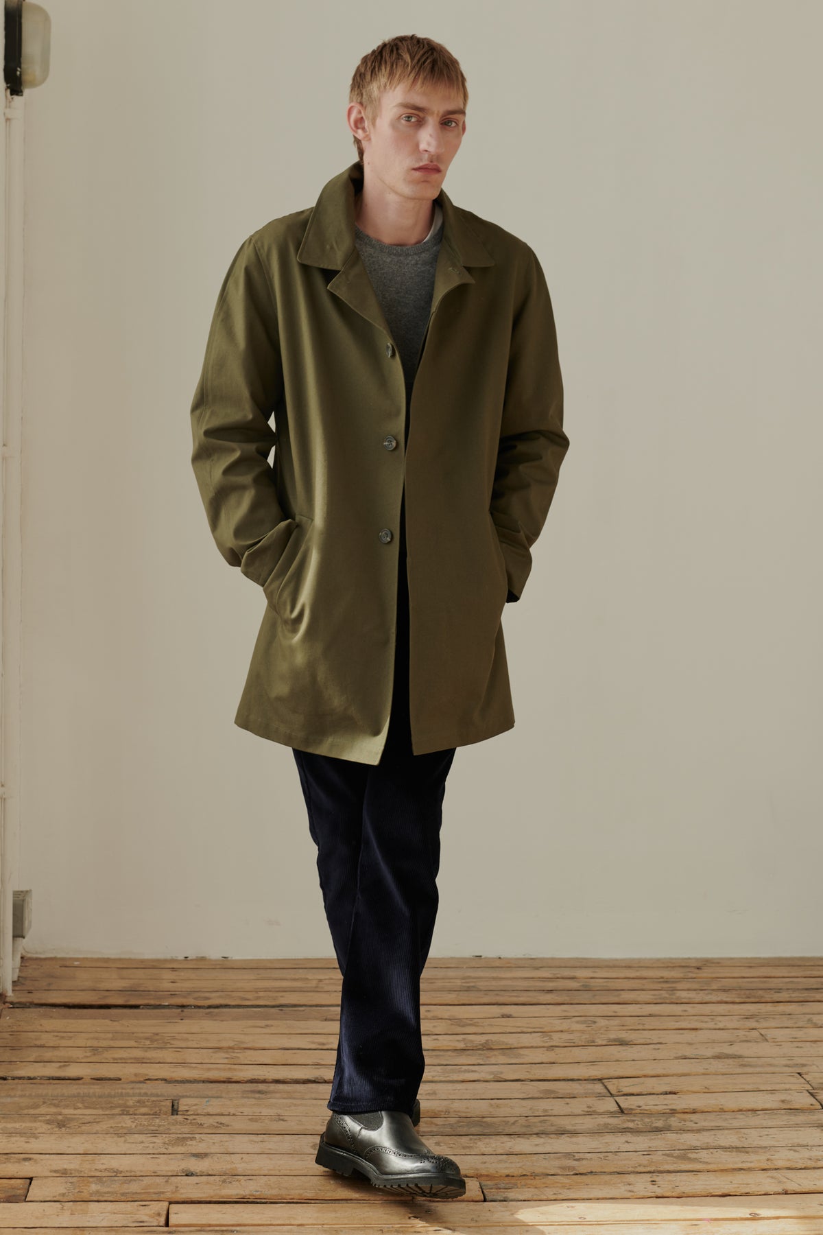 
            Full body image of male wearing men&#39;s raincoat in olive. 2 side welt pockets. Concealed button placket. Half lined